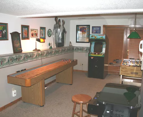 Game room with a shuffleboard table, arcade game, and framed artwork.