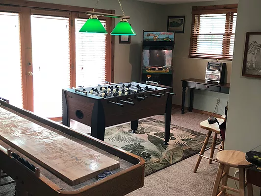 Game room with foosball table, shuffleboard, arcade game, bar area, and sliding glass door.