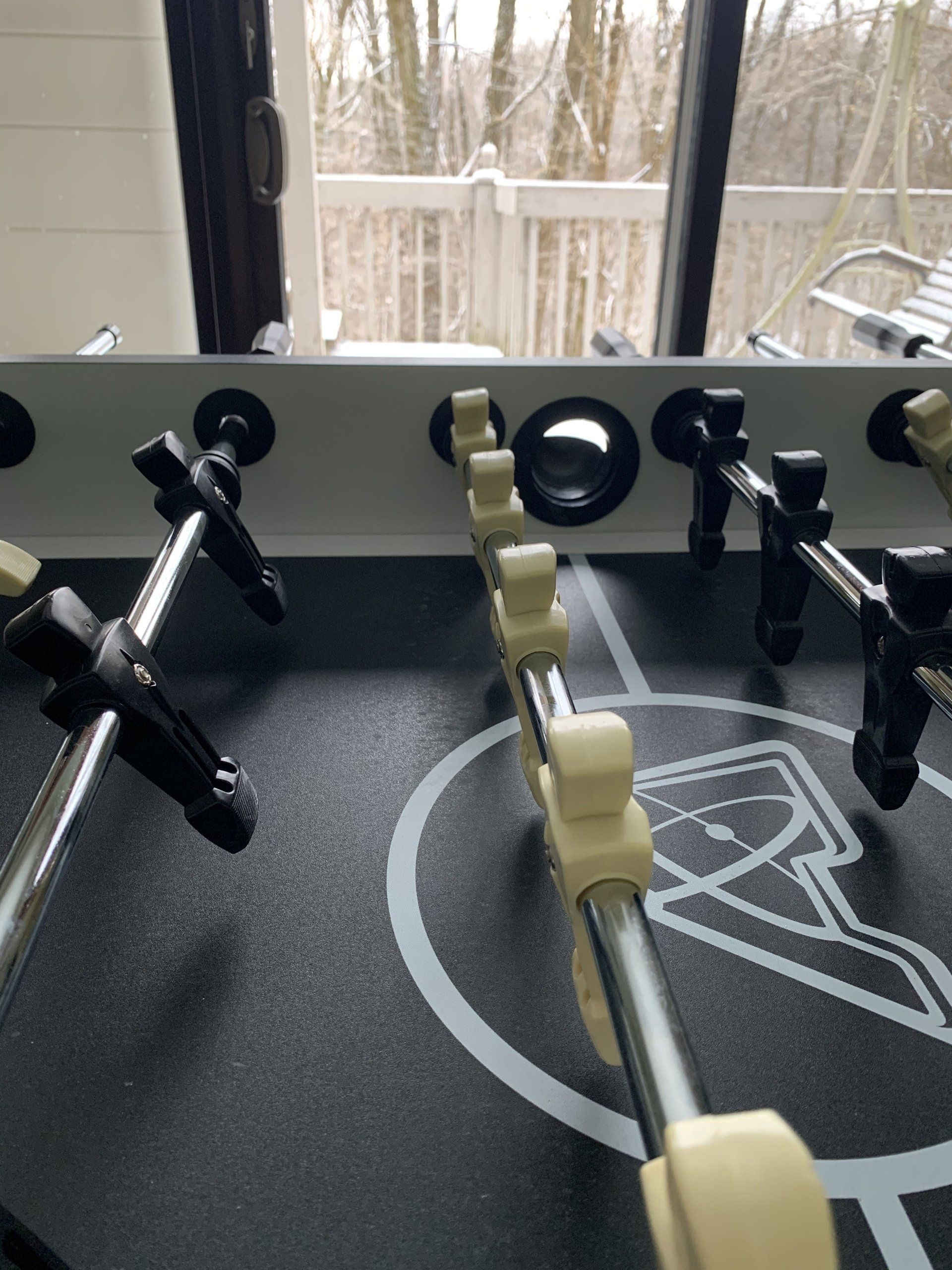 Foosball table with black and white players, viewed from the inside with an outdoor deck view in the background.