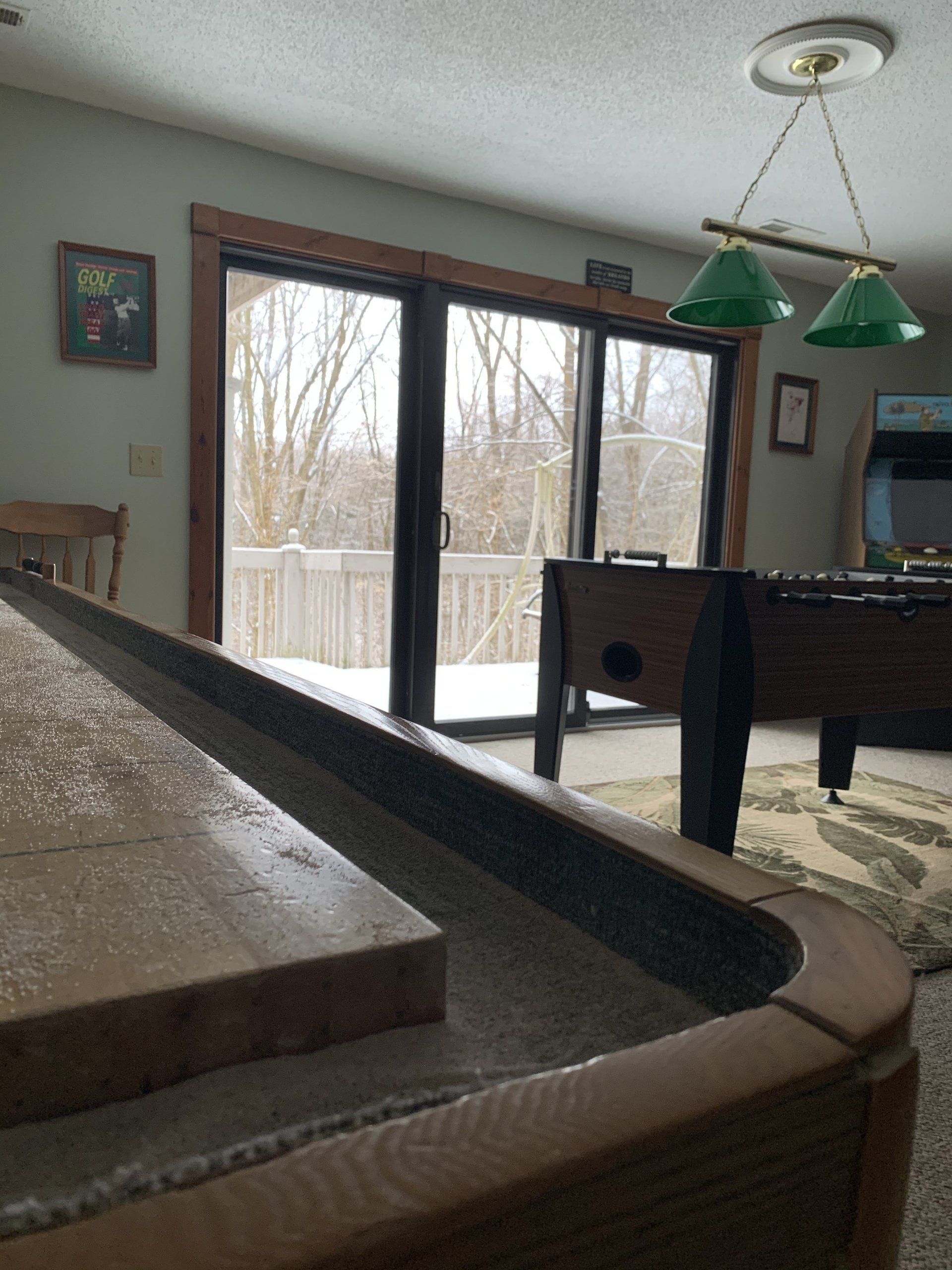 Indoor recreation room with a shuffleboard table, foosball table, and a sliding glass door.