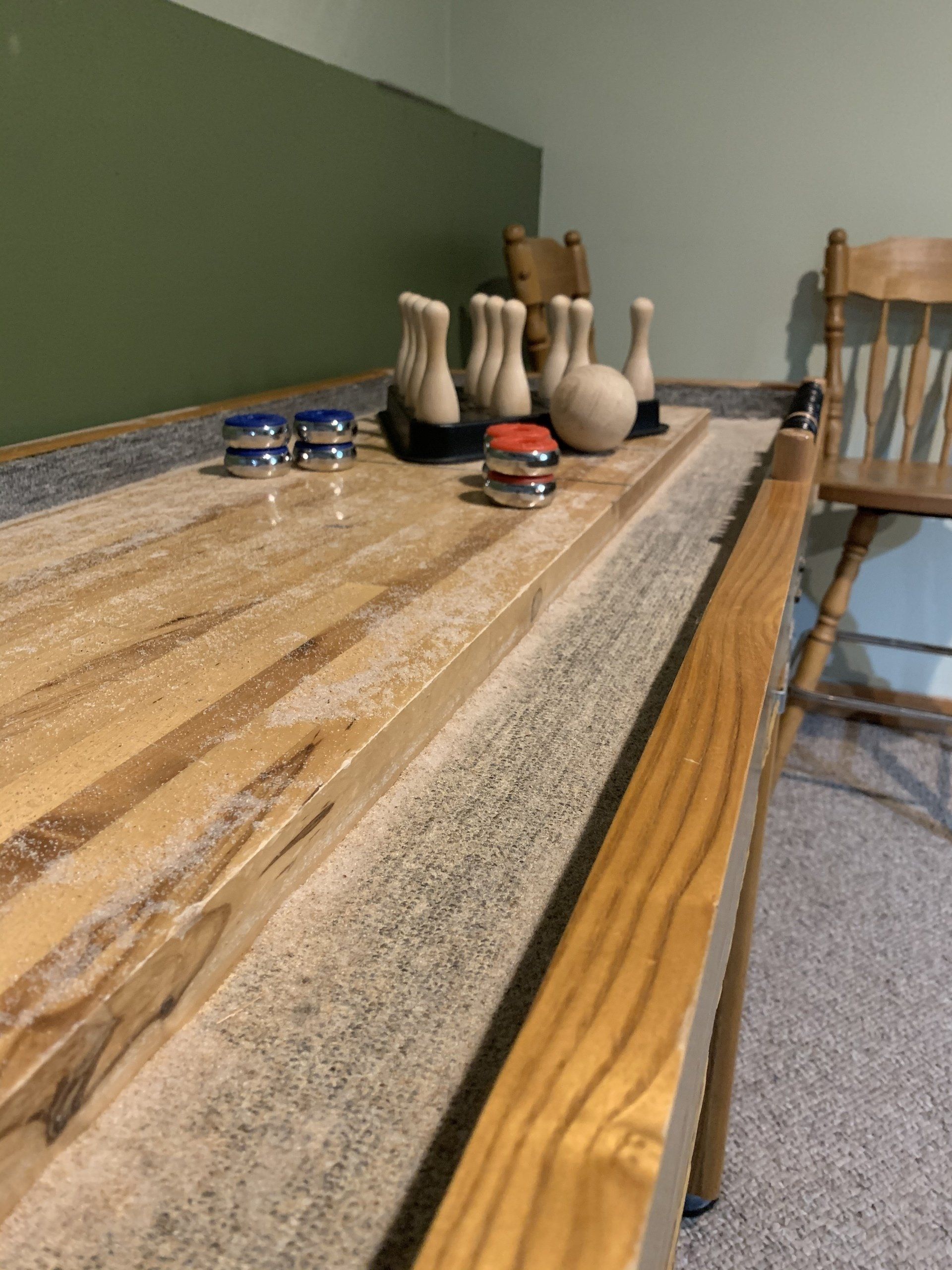 Shuffleboard game with wooden surface, pins, and pucks. Interior setting, green wall.
