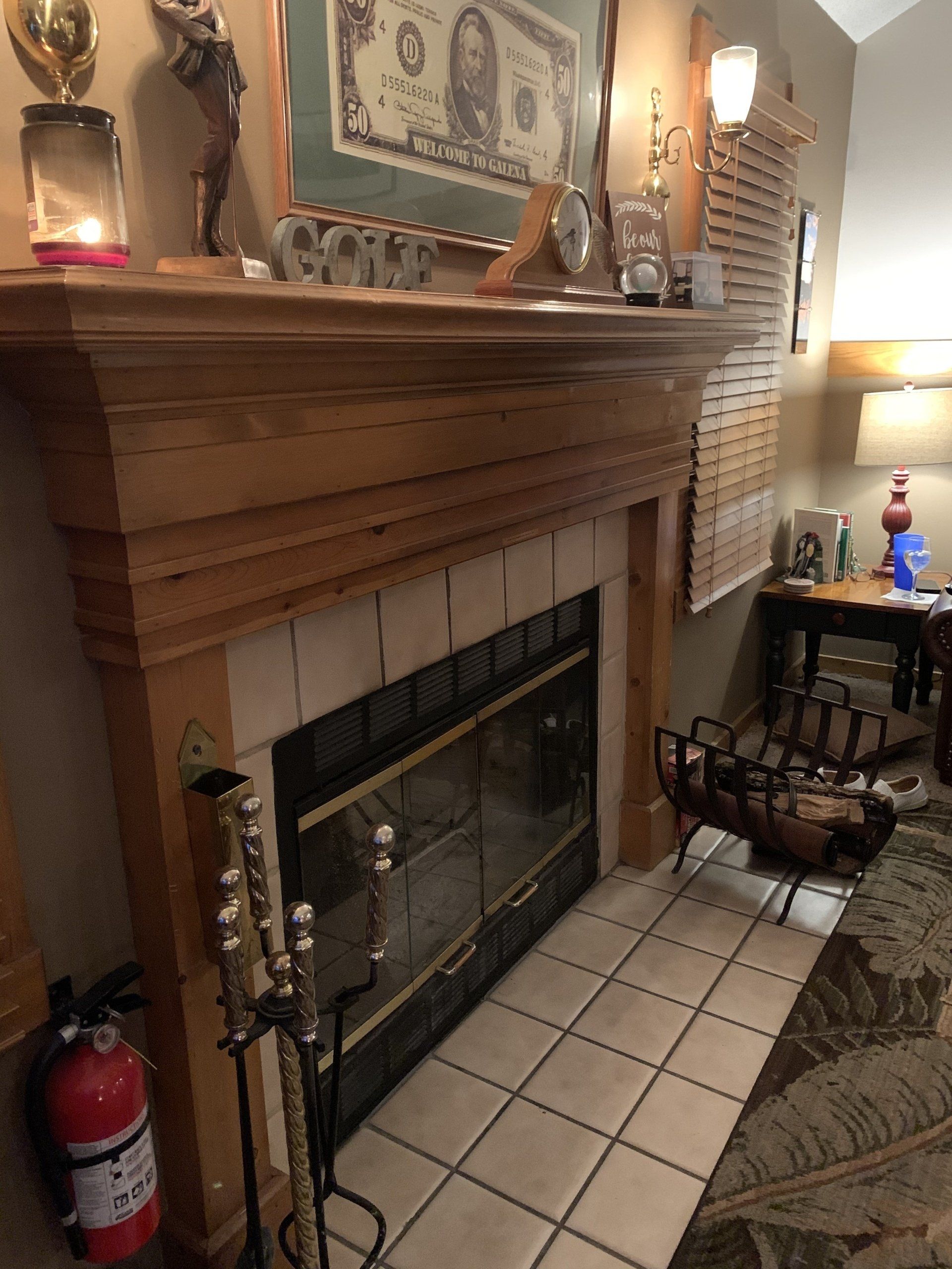 Fireplace with wooden mantel, tile hearth, fire tools, fire extinguisher, and various decorations.