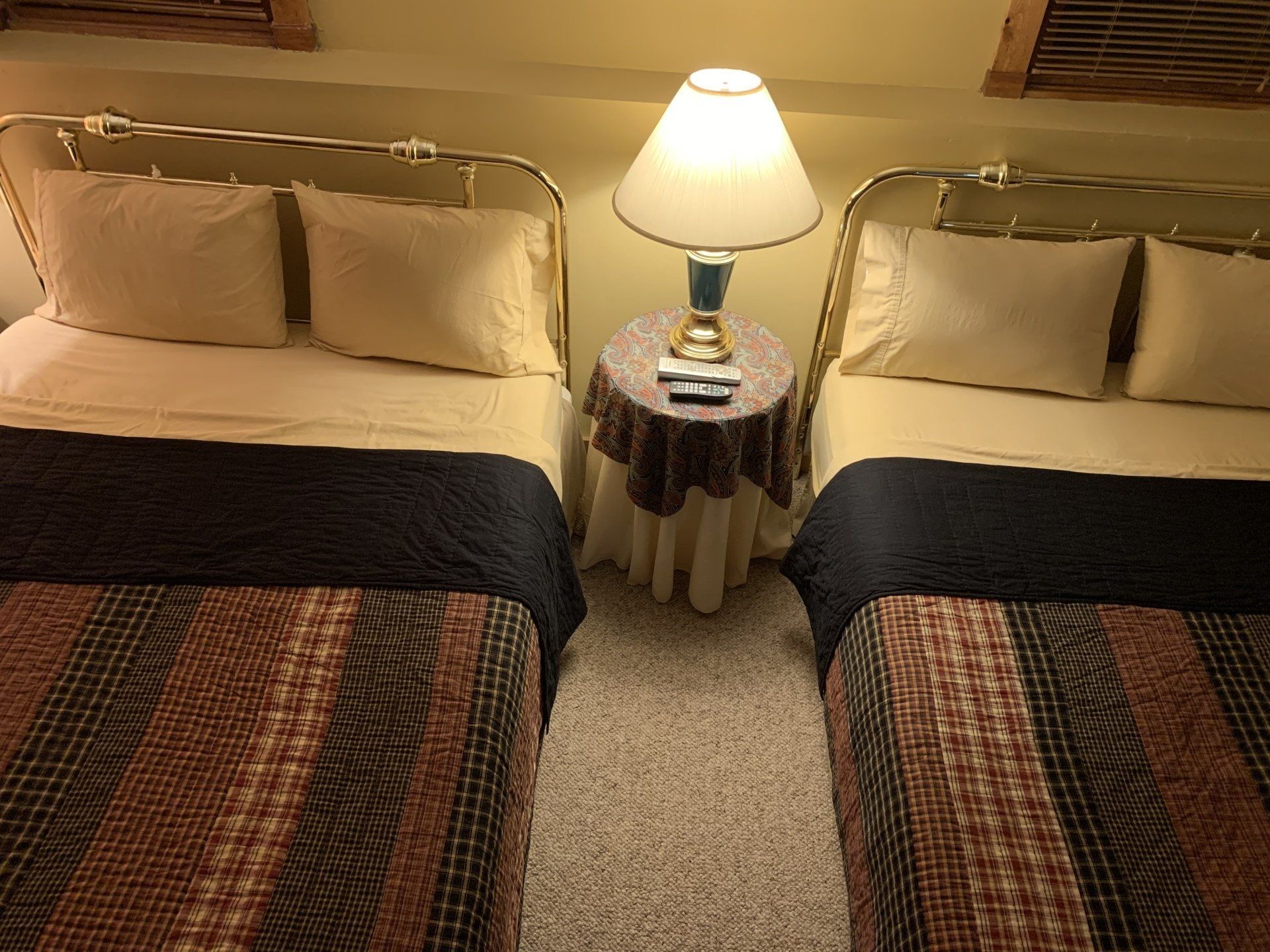 Two twin beds with patterned blankets, nightstand with lamp, beige walls.