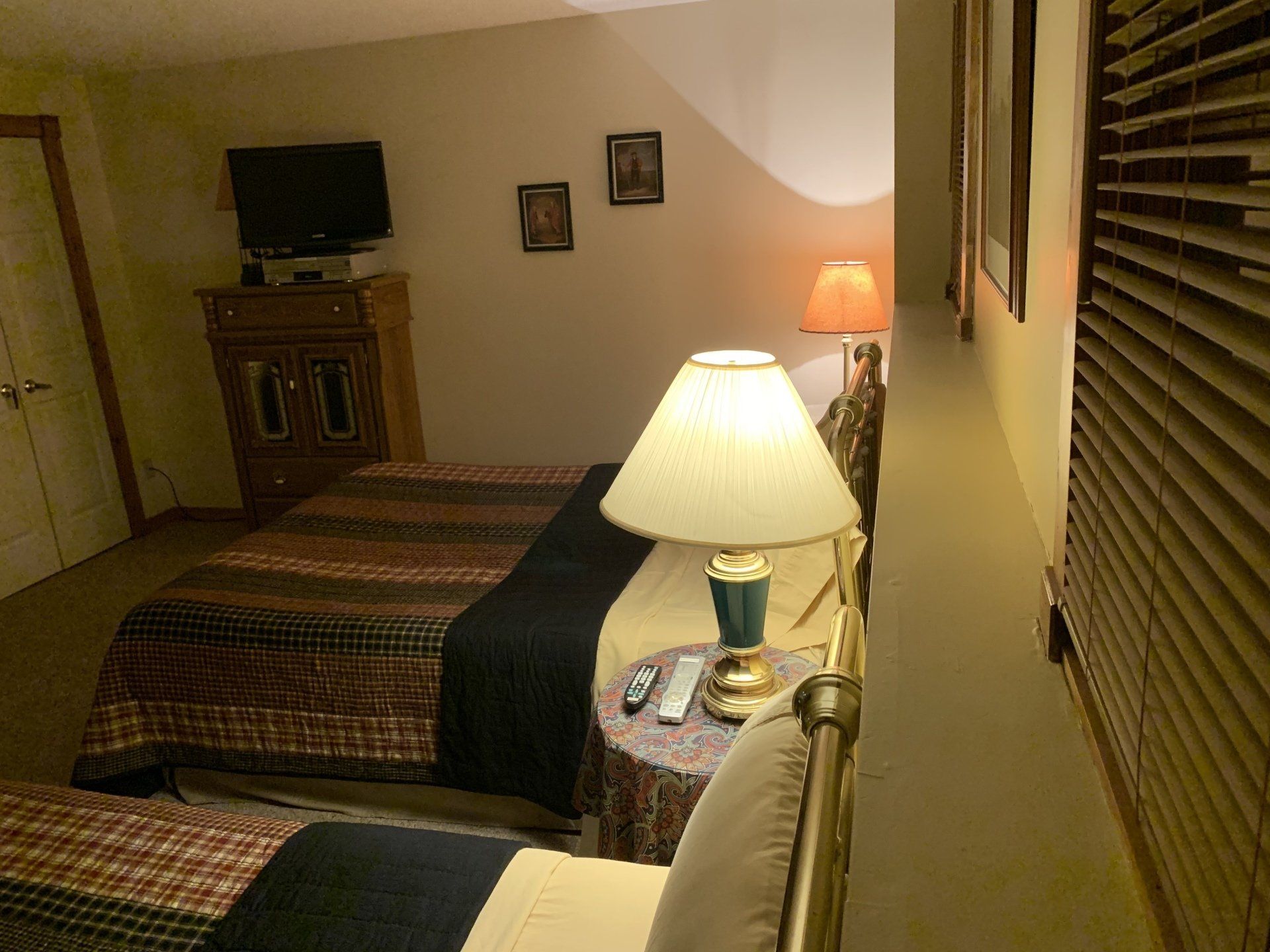 Bedroom with two beds, lamps, TV on a dresser, and wall art. Dark, patterned bedding.