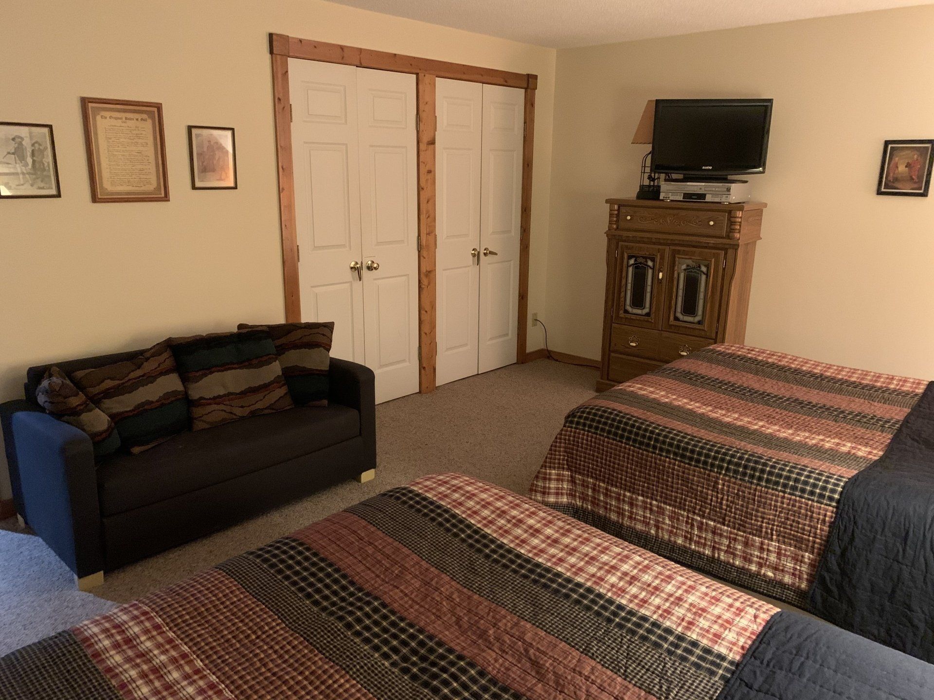 Bedroom with two beds, small sofa, dresser with TV, and closet. Brown, tan, and blue tones.