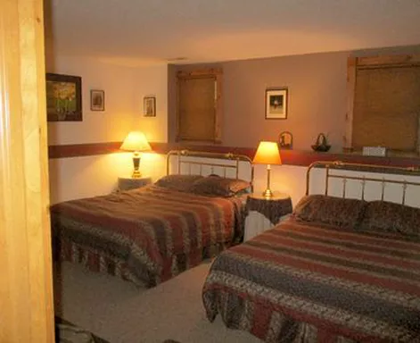 Two beds in a room with lamps and small artwork on walls.