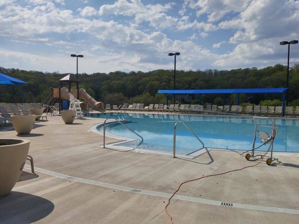 Swimming pool with a slide, blue canopy, and lounge chairs on a sunny day.