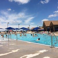 Outdoor swimming pool on a sunny day with people swimming. Blue umbrellas, building in the background.