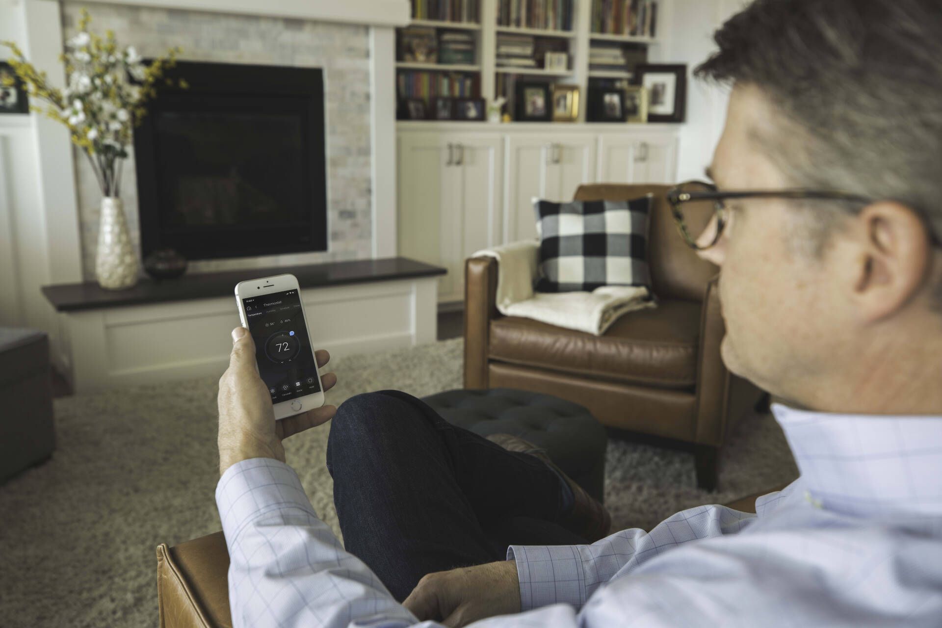 A man is sitting in a living room holding a cell phone.