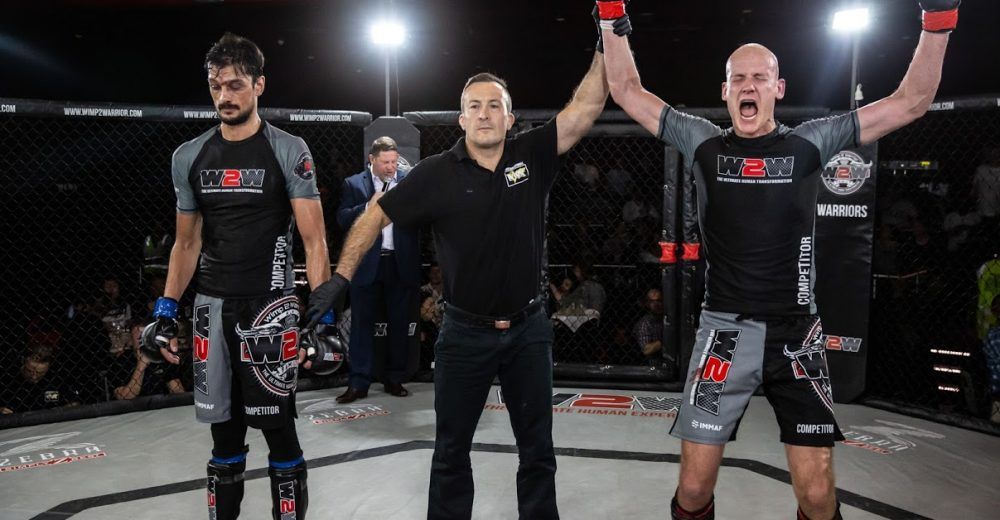 Two MMA fighters stand with a referee as one raises both arms in victory in the cage.