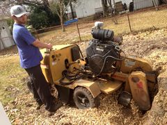A man is working on a stump grinder in a yard