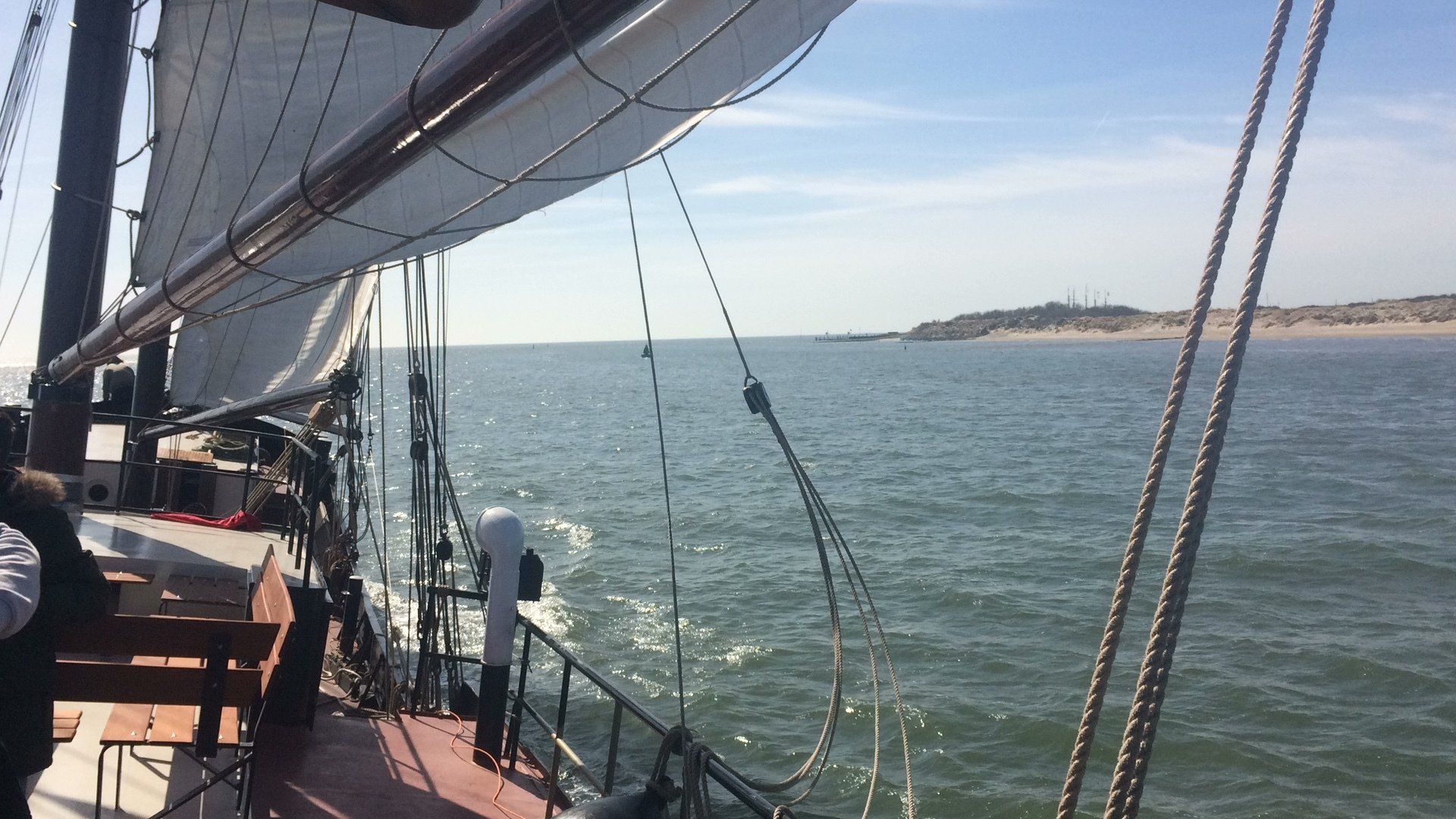 View from the deck with ropes and sails, sailing along the Dutch coast in the Netherlands.