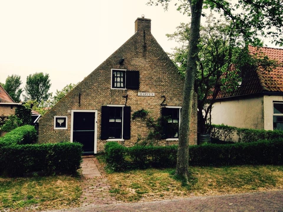 Charming island house in the Dutch Wadden Islands with dark door, shutters and neatly trimmed hedges.