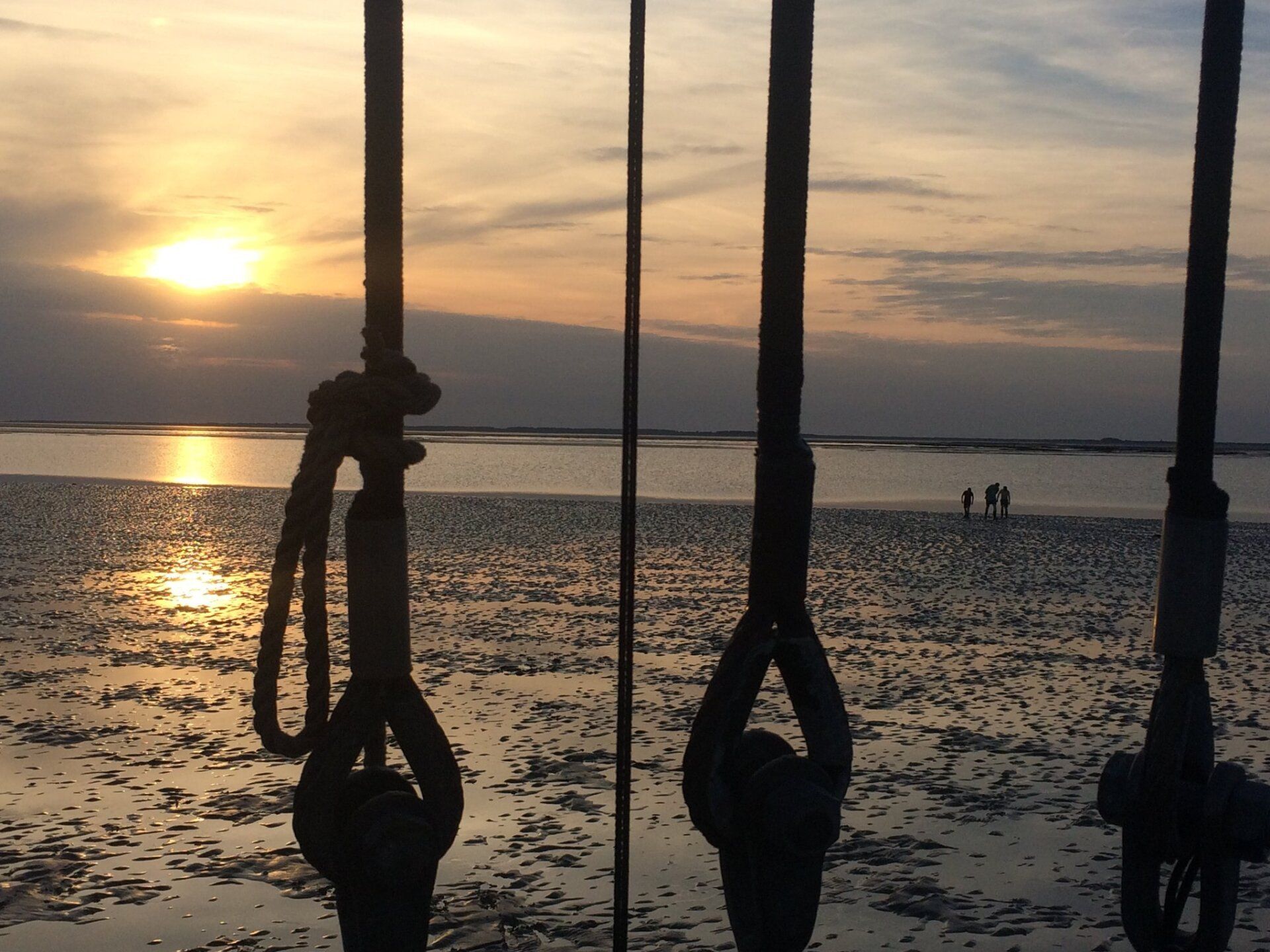 Sunset walk along the waterline seen through ship rigging, on the Dutch Wadden Sea tidal flats.