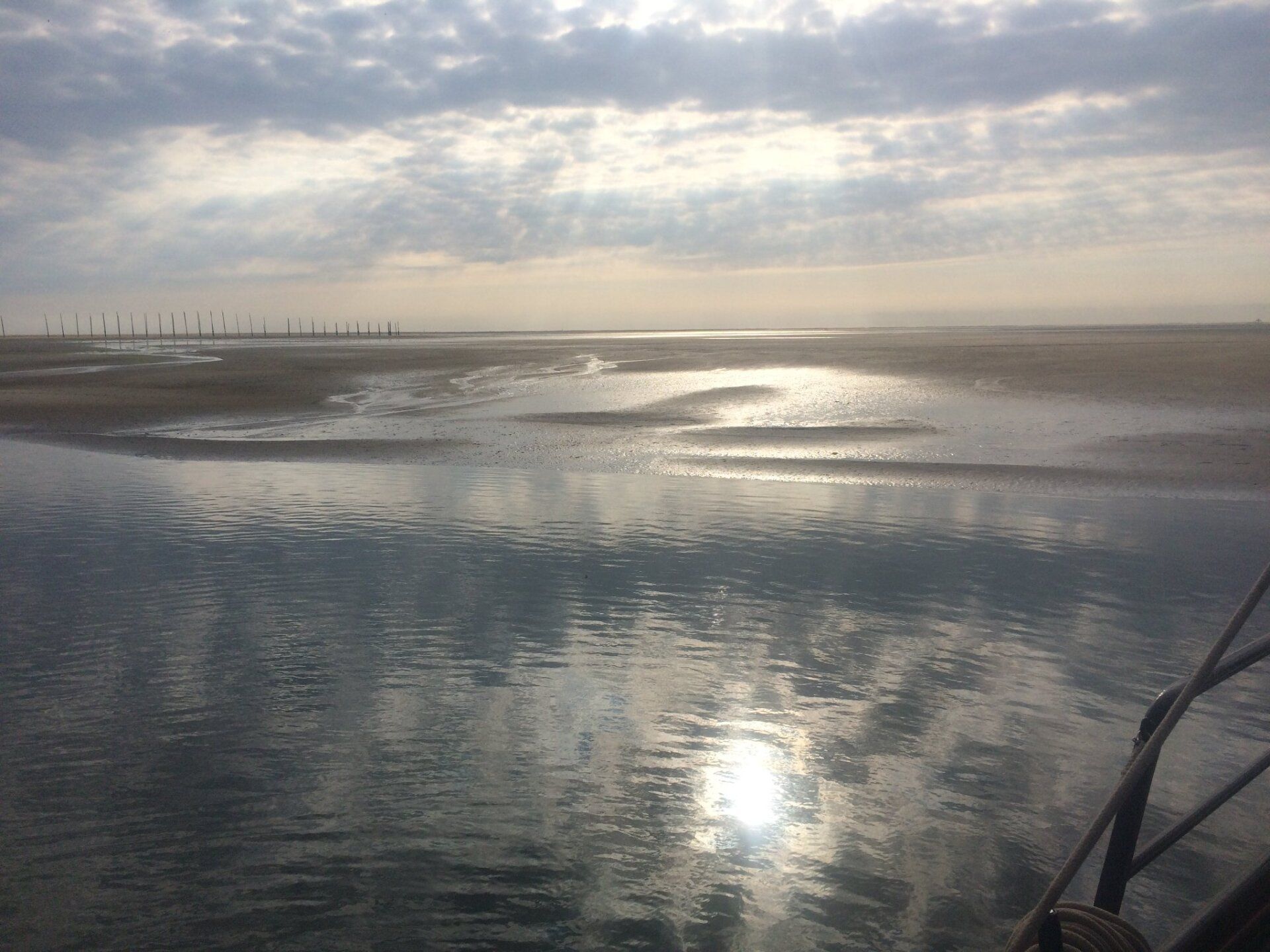 Mirror-calm water reflecting clouds and sunlight, with a Wadden Sea sandbank in the distance.
