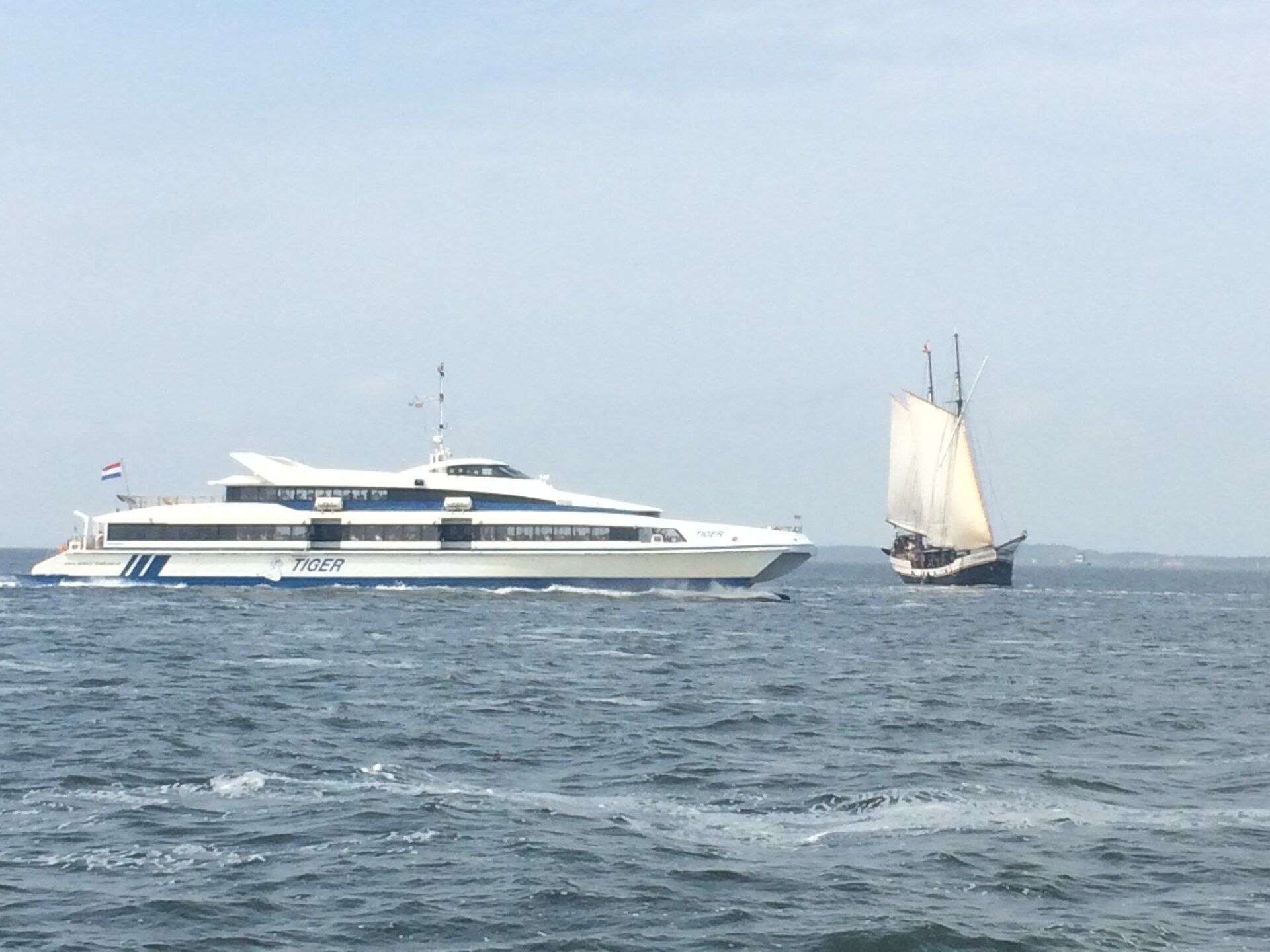 Large ferry passing a small sailboat at sea in the Netherlands, a typical Wadden Sea crossing view.