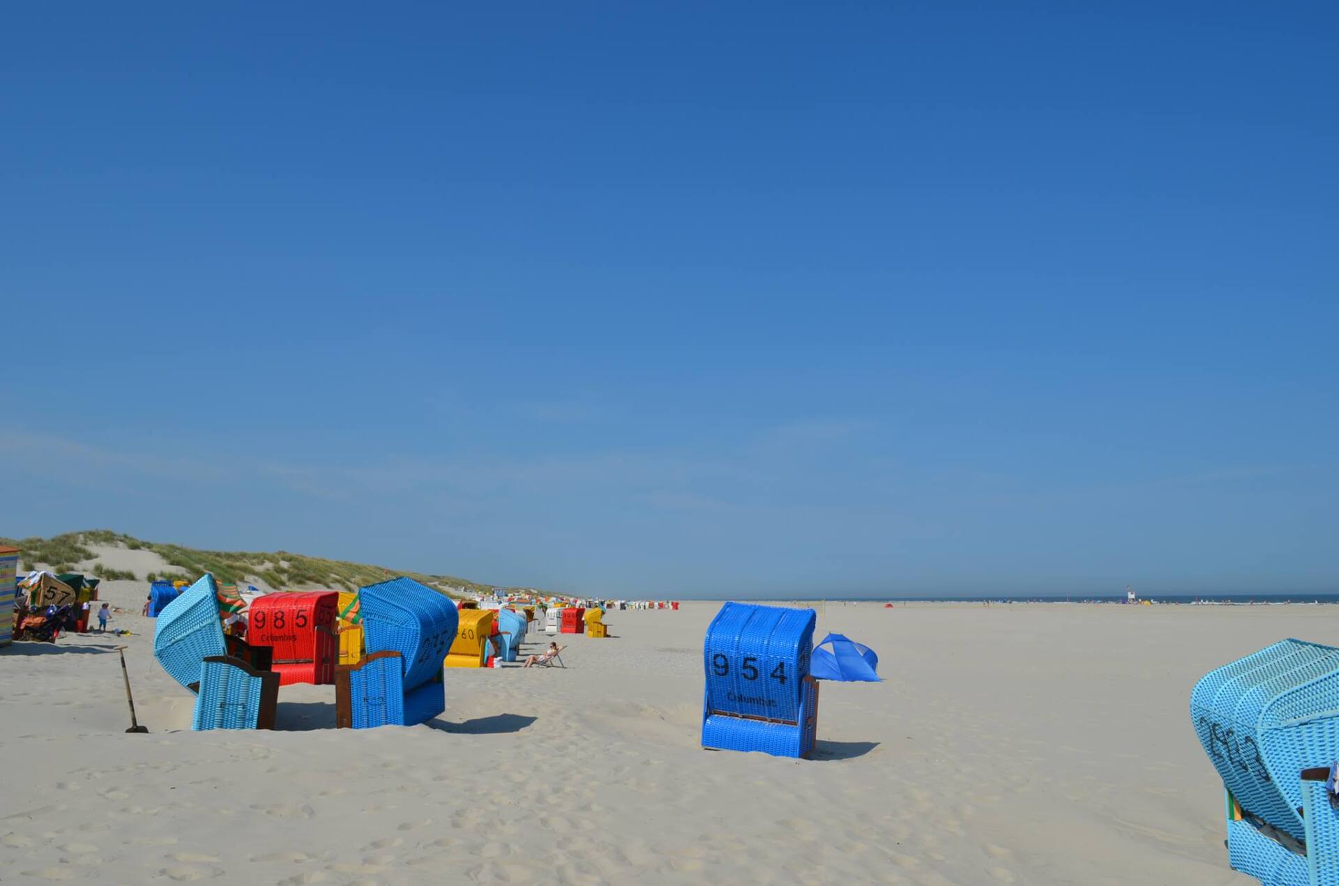 Colourful beach umbrellas under a clear blue sky on a sunny day in the Dutch Wadden Islands.