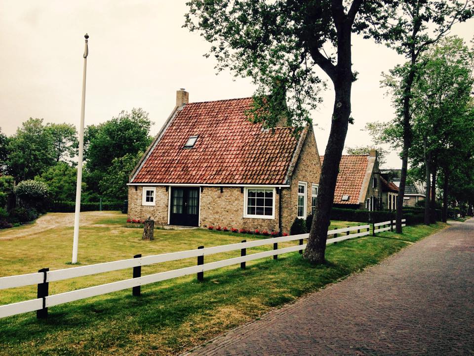 Island home with red-tiled roof, white fence and flagpole under a cloudy sky in the Dutch Wadden Islands.
