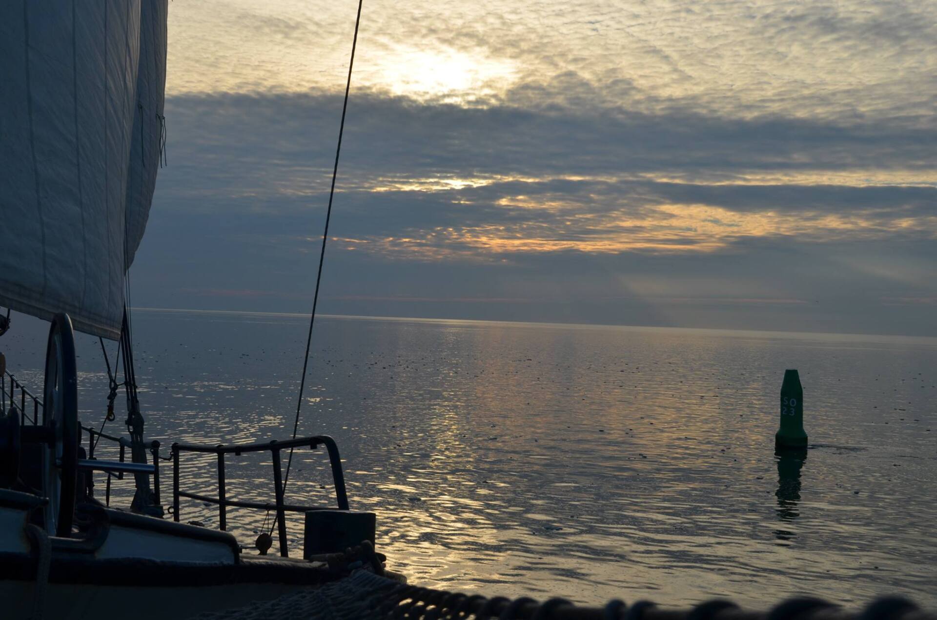 Sailing ship at sunrise on calm water in the Dutch Wadden Sea, with a green buoy in the distance.