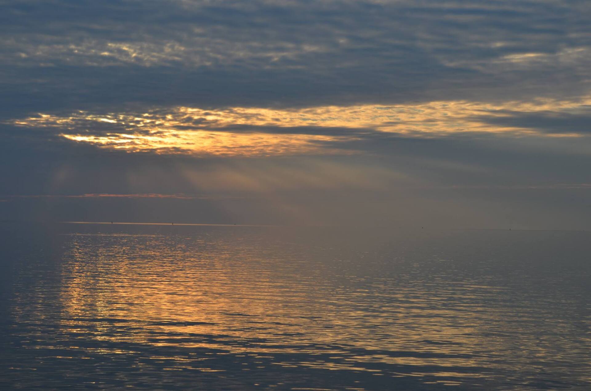 Golden sunlight breaking through clouds and sparkling on the sea near the Dutch Wadden coast.