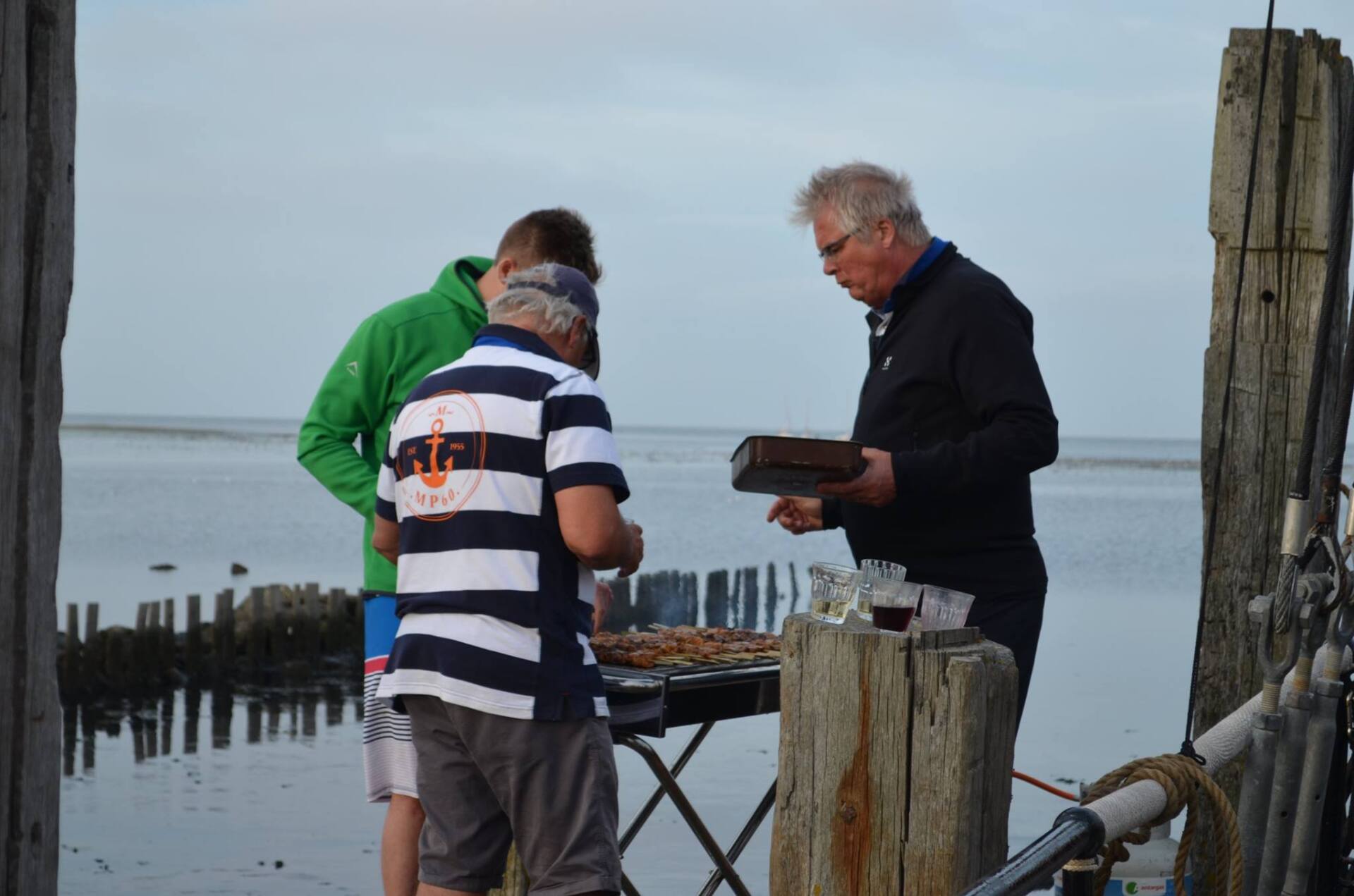 Outdoor barbecue by the water on the Dutch Wadden Sea, friends cooking and enjoying the view.