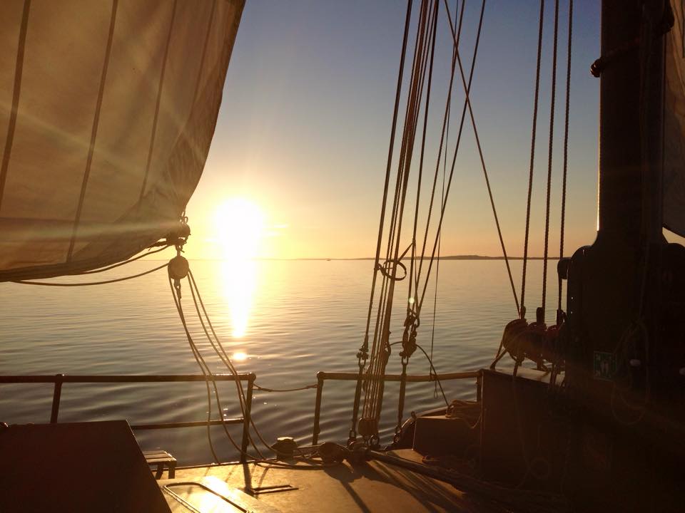 Sunset from the deck with ropes and sails, reflecting on the water during a Dutch Wadden Sea sailing trip.