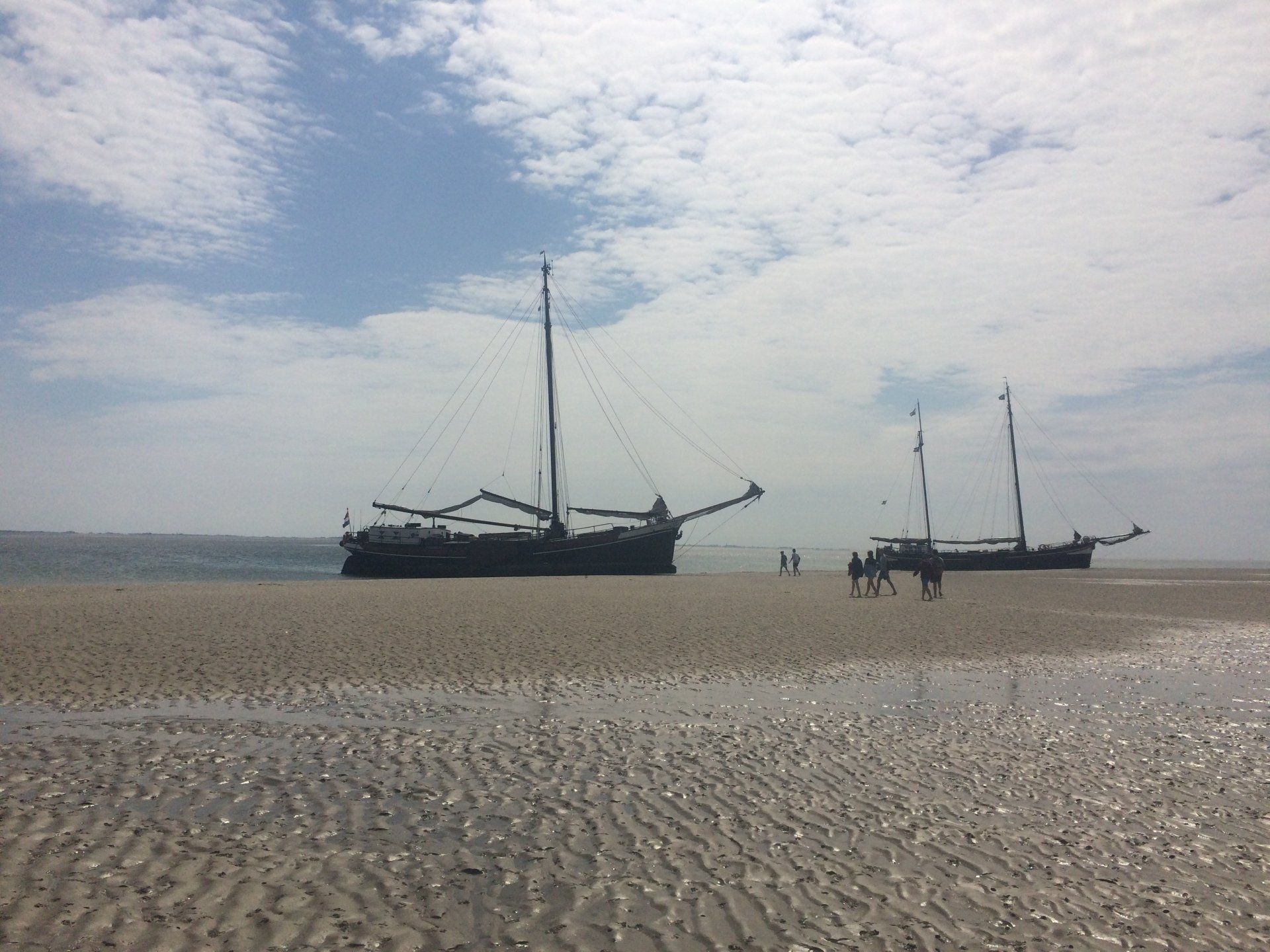 Two traditional sailing ships at the beach with people walking around under overcast skies in the Netherlands.