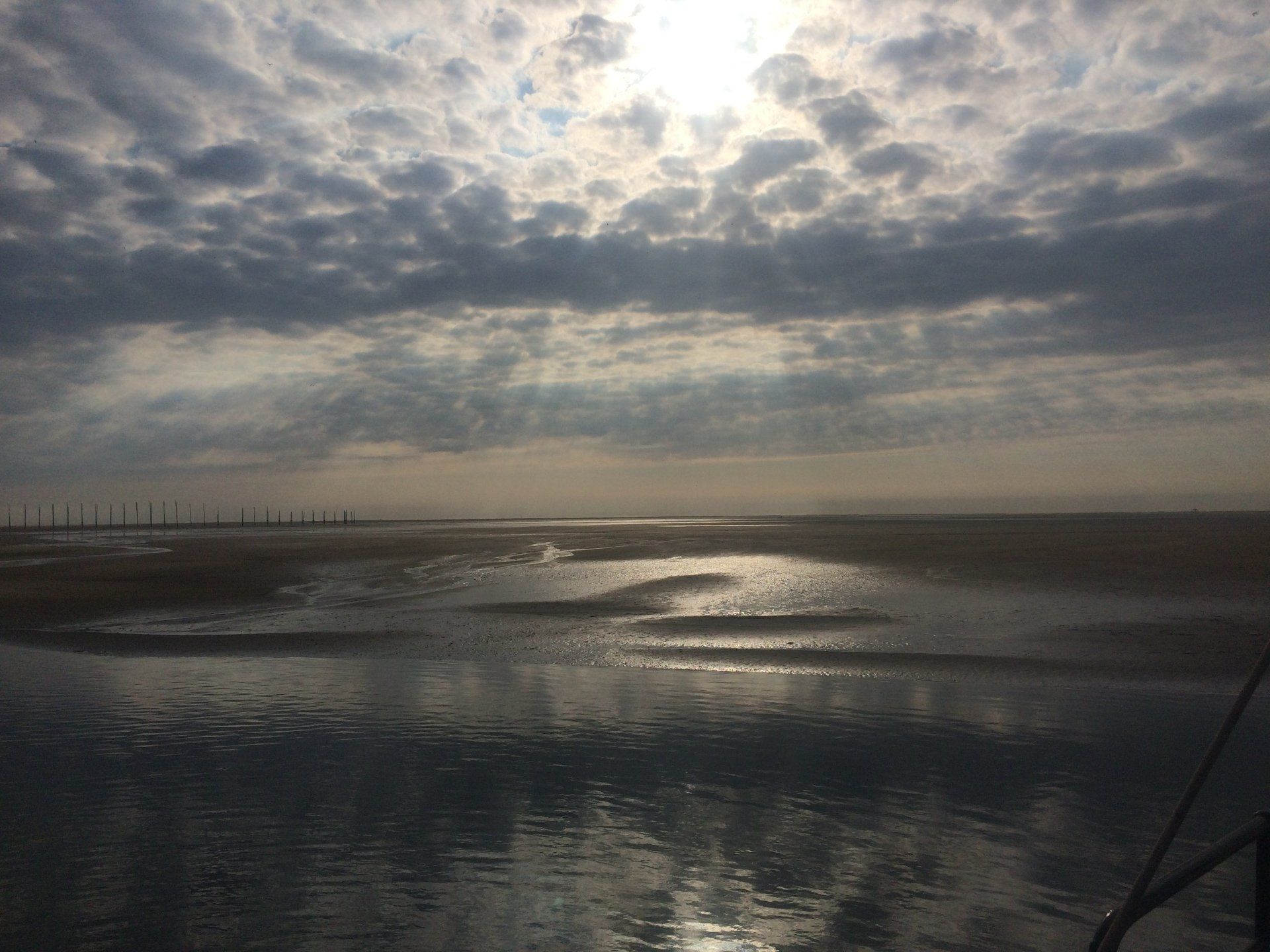Cloudy sky above a wet sandbank, with sunlight breaking through and reflecting on the Wadden Sea.