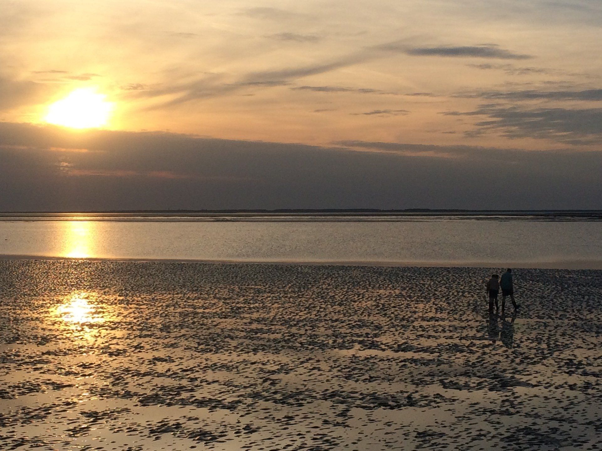 Sunset walk on the beach with reflections in wet sand, two figures in the distance in the Dutch Wadden region.