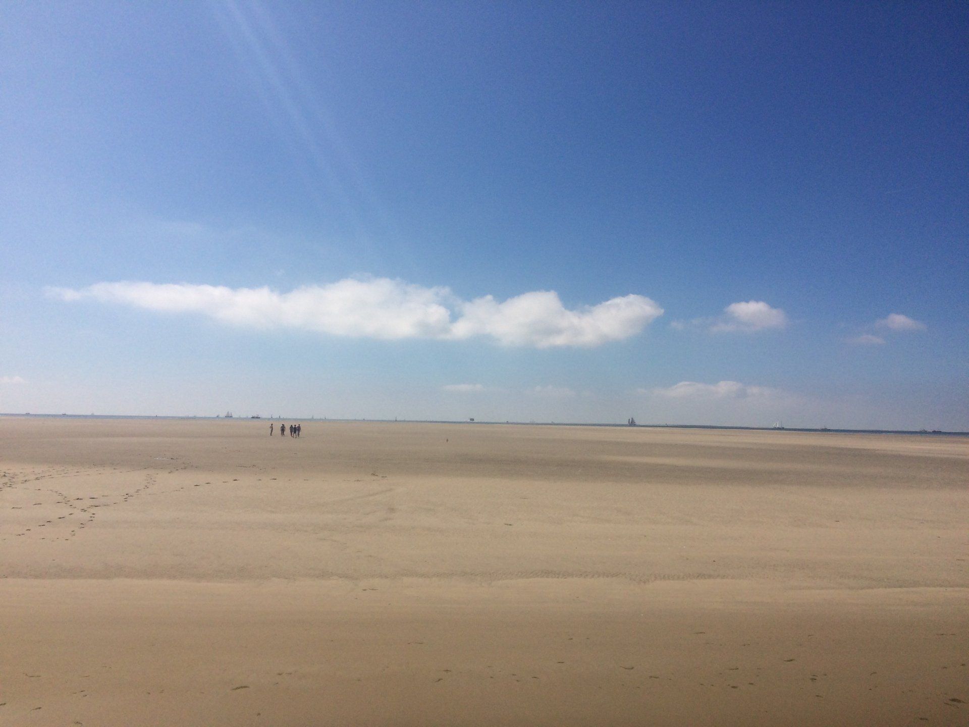 Beach under a clear blue sky with people walking along the coast in the distance, Dutch Wadden Islands.