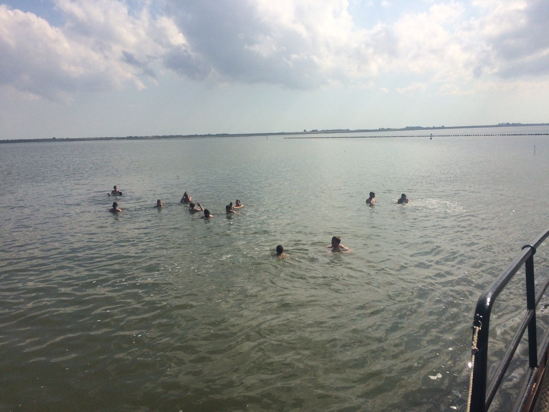 Open-water swim near a sailing ship in the Netherlands on an overcast day, viewed from the ship’s edge.