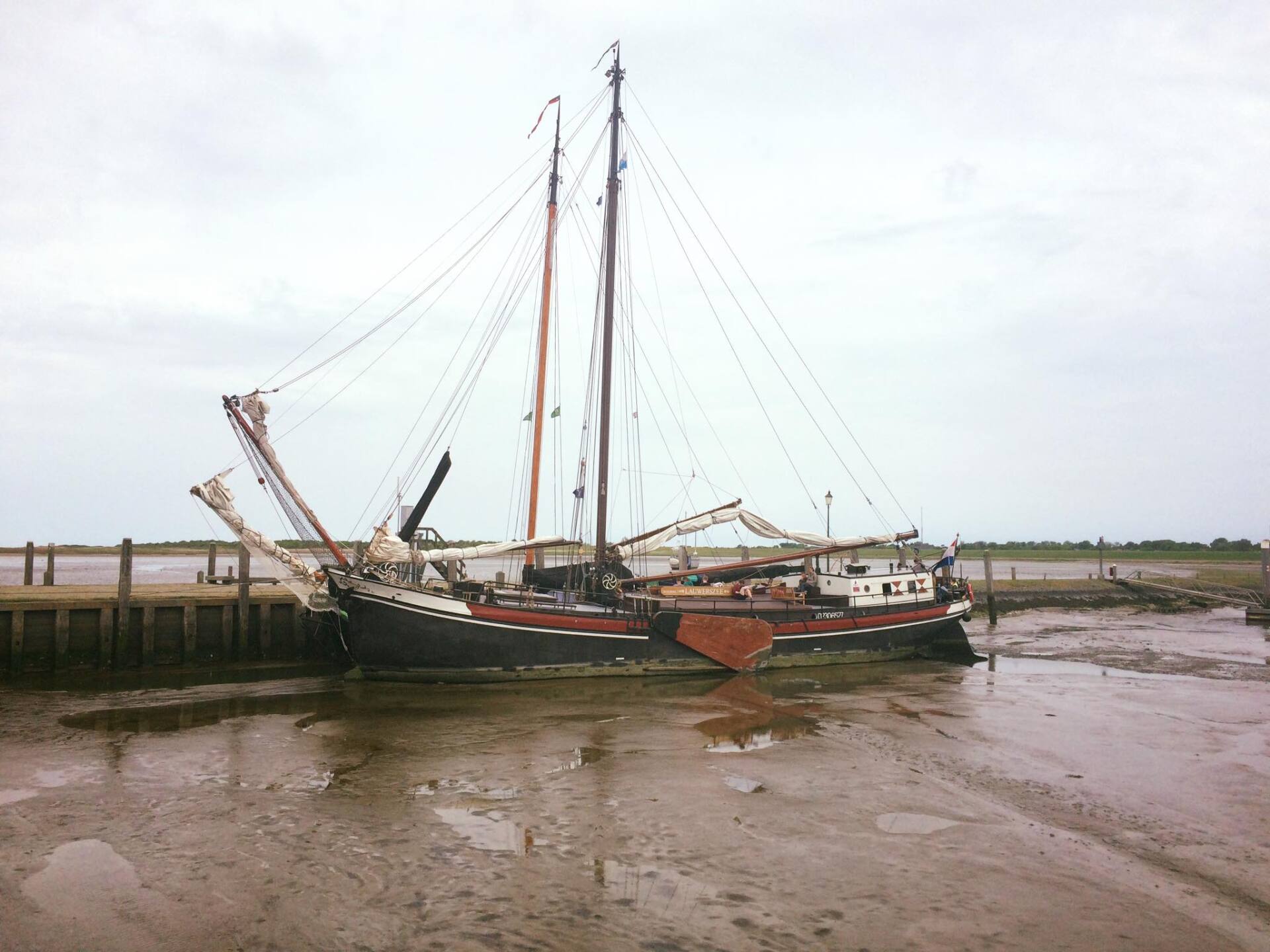 Sailing ship grounded in mud at low tide near a pier, showing the tidal range of the Dutch Wadden Sea.