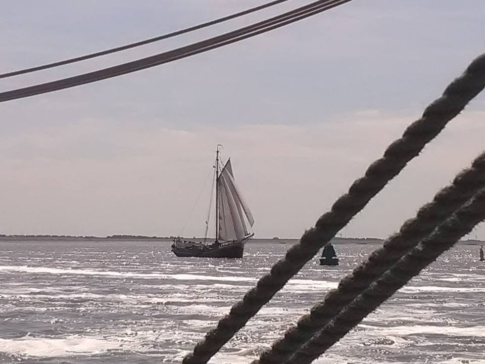 Sailing ship seen through thick ropes on a cloudy day, classic Dutch maritime atmosphere.