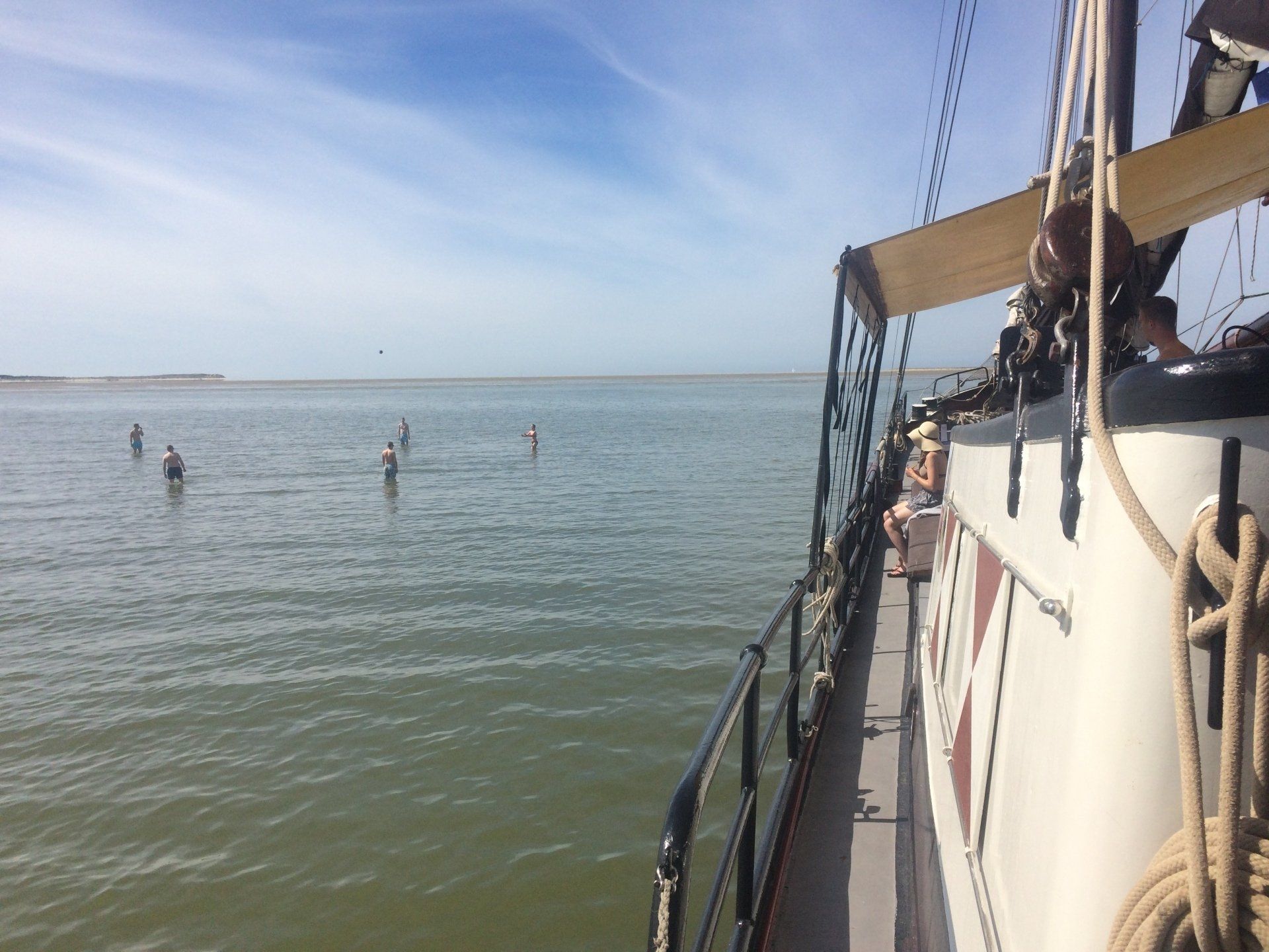 Sailing ship on the water with mudflat walkers in view under a blue sky in the Dutch Wadden Sea.