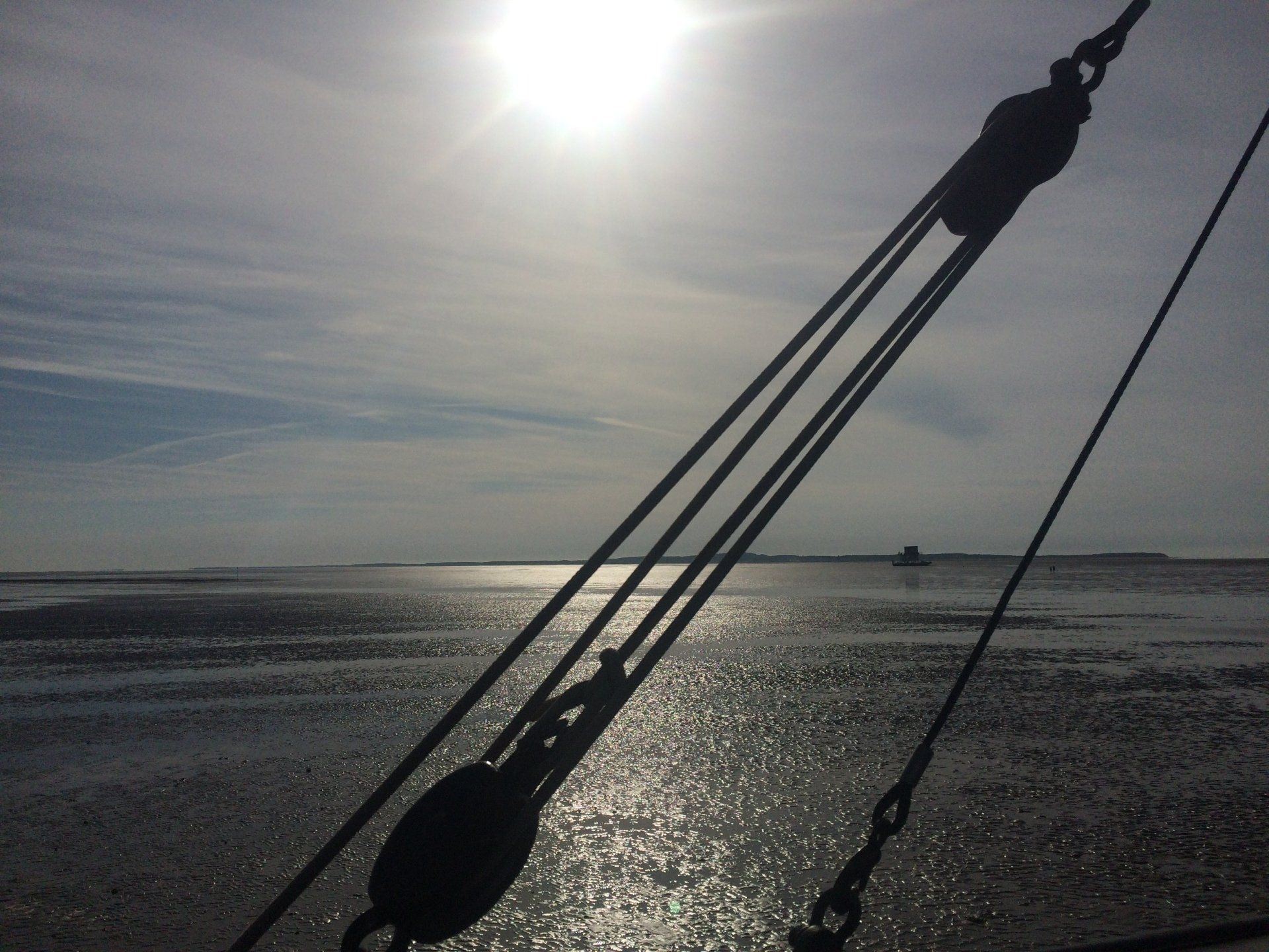 Silhouette of ship rigging against a sunlit Wadden Sea landscape at low tide in the Netherlands.