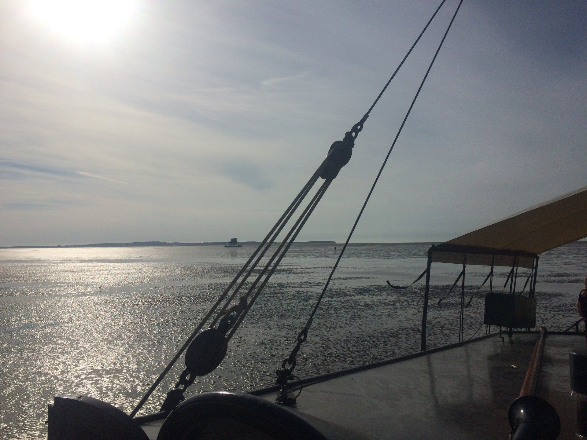Sunlight on the water with ship rigging silhouetted against the sky and an island in the distance in the Netherlands.