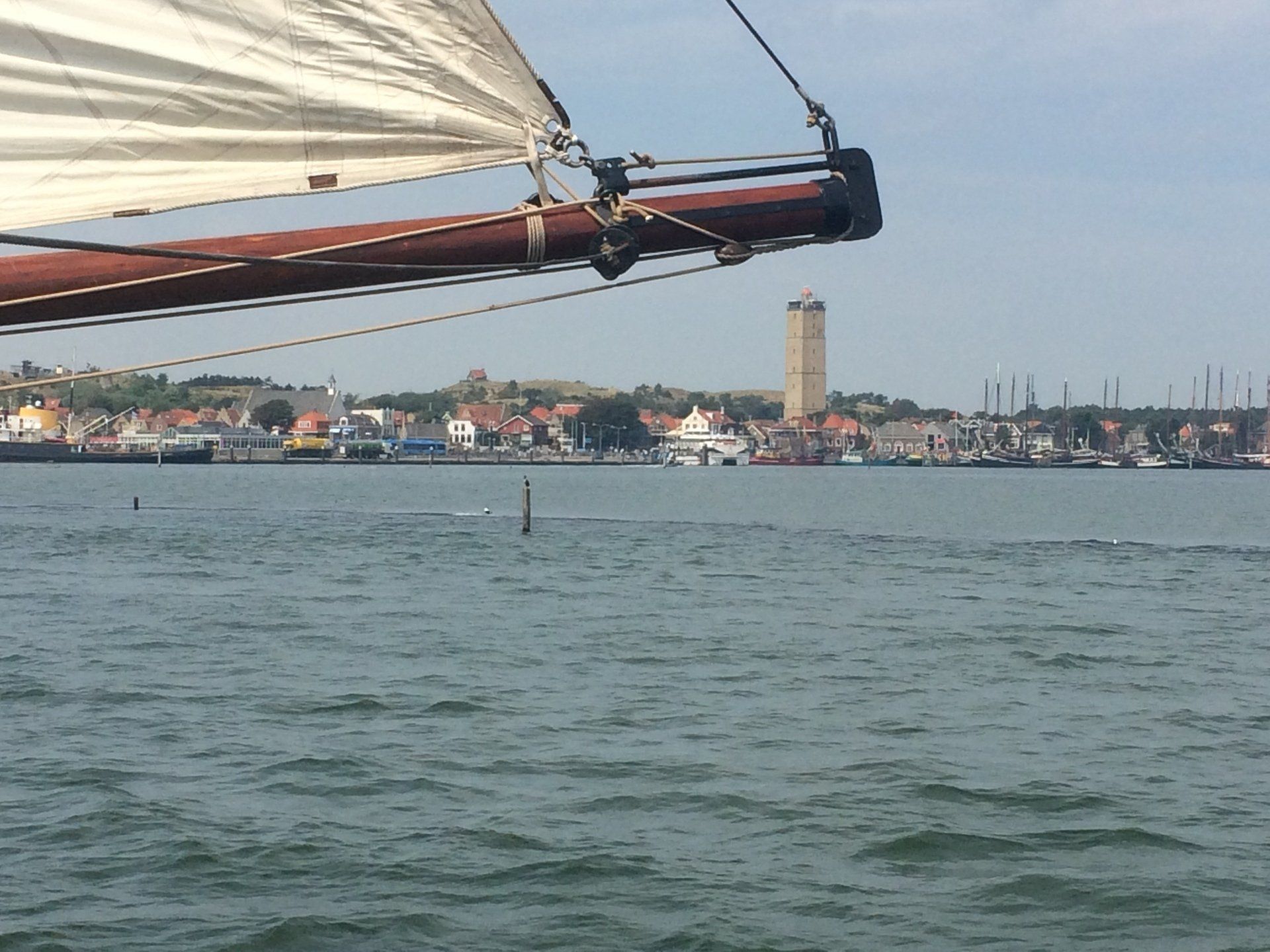 Sailing ship passing a coastal town with a tall church tower on a sunny day in the Netherlands.
