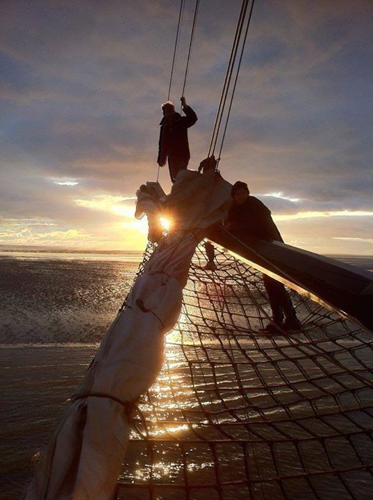 Crew on the bow at sunset, waves breaking with the sun shining through the rigging on the Dutch Wadden Sea.