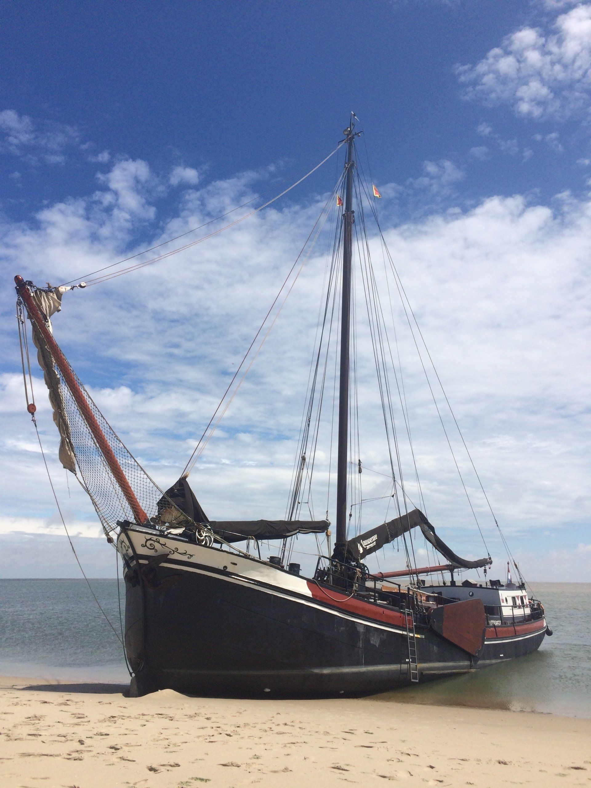 Traditional sailing ship dried out on sand under a blue sky with light clouds on the Dutch Wadden Sea.