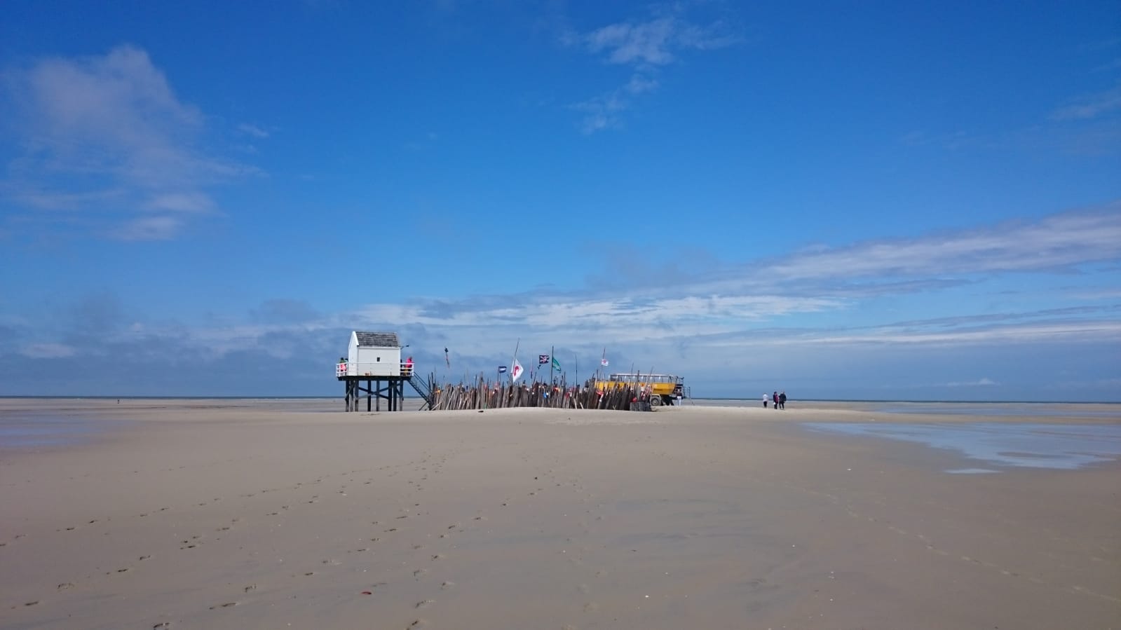 People gathering by a beach building under a deep blue sky on a Dutch Wadden Island.
