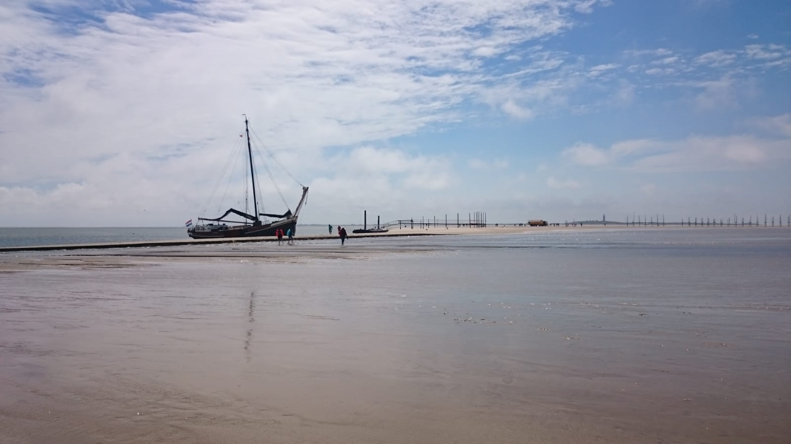 Sailing ship resting on a sandbank near the waterline under soft clouds in the Dutch Wadden Sea.