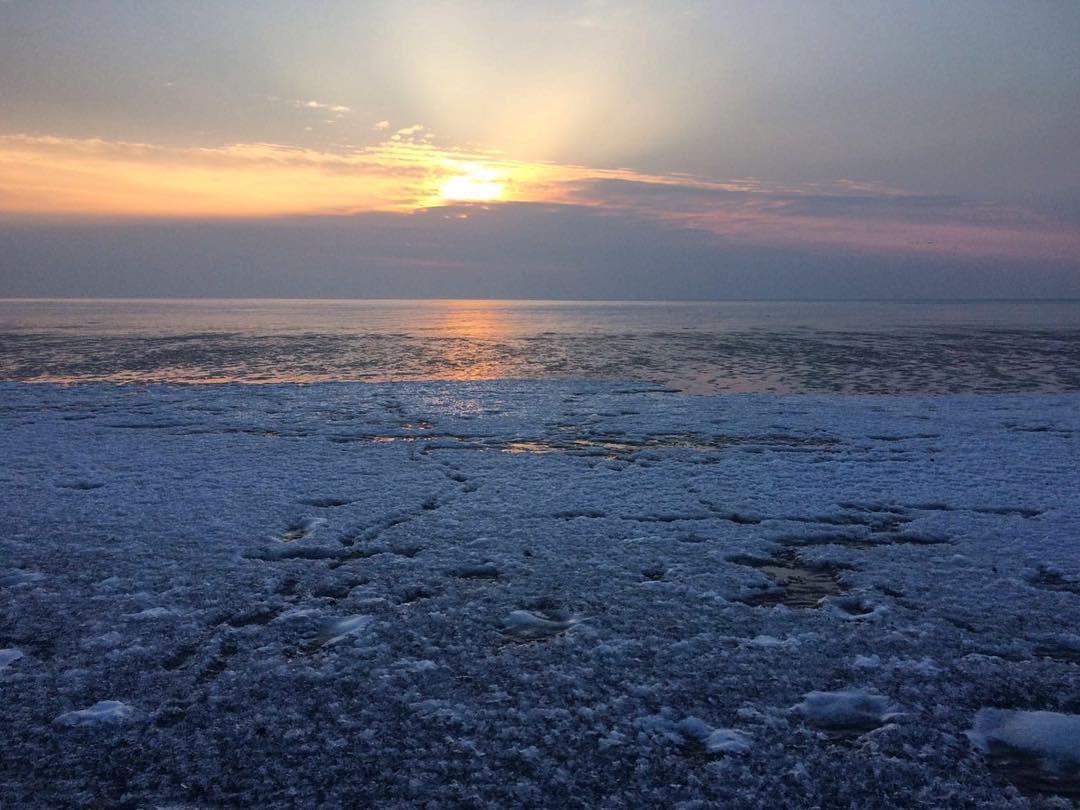 Winter sunrise with ice in the foreground, orange and blue tones over water in the Netherlands.
