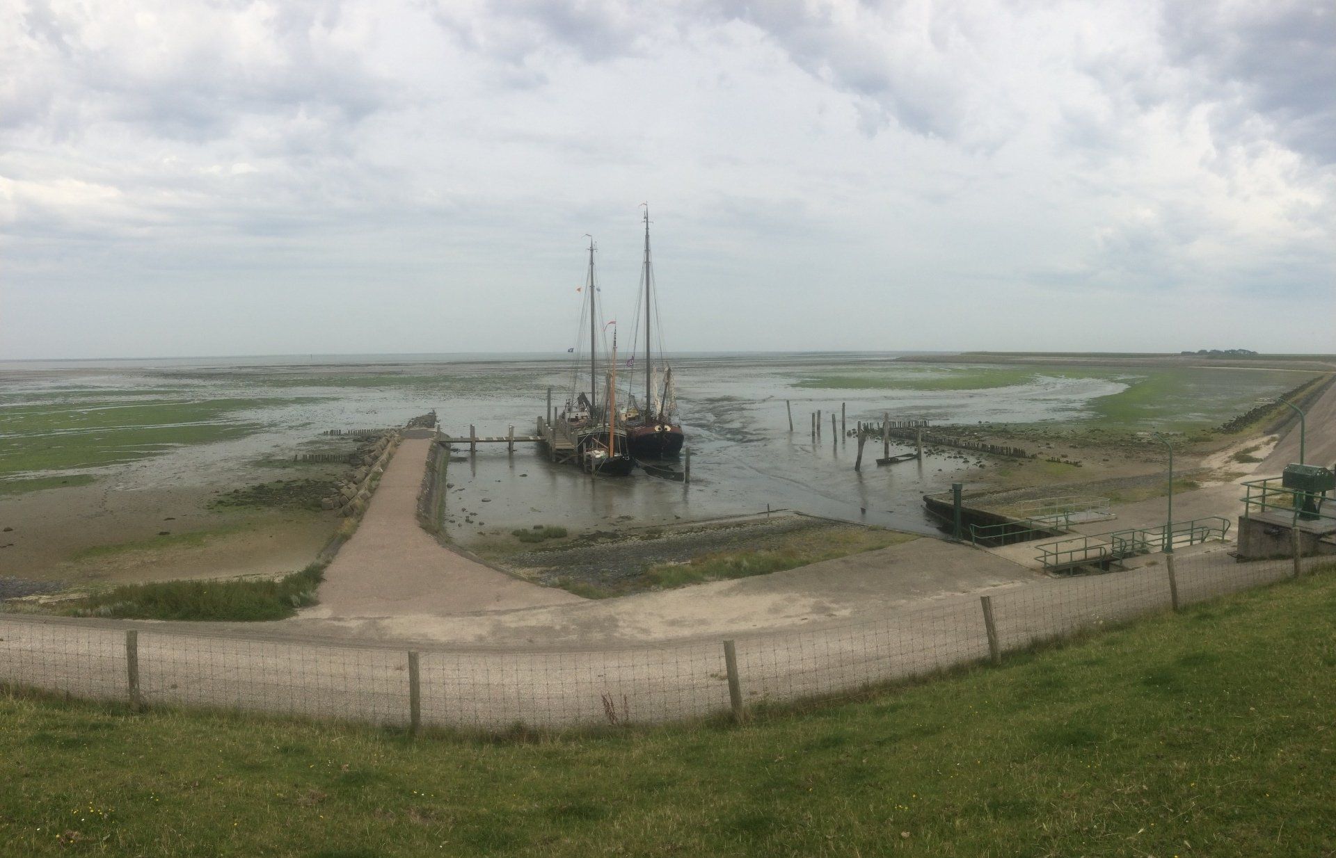 Sailing ship in a harbour at low tide, surrounded by wide mudflats and salt marshes in the Dutch Wadden Sea.