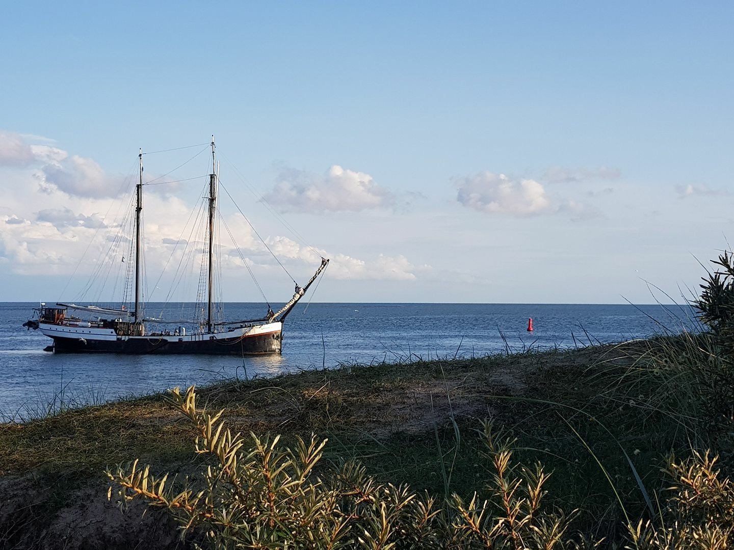 Sailing ship near a low, green shoreline under a blue sky in the Dutch Wadden Sea region.