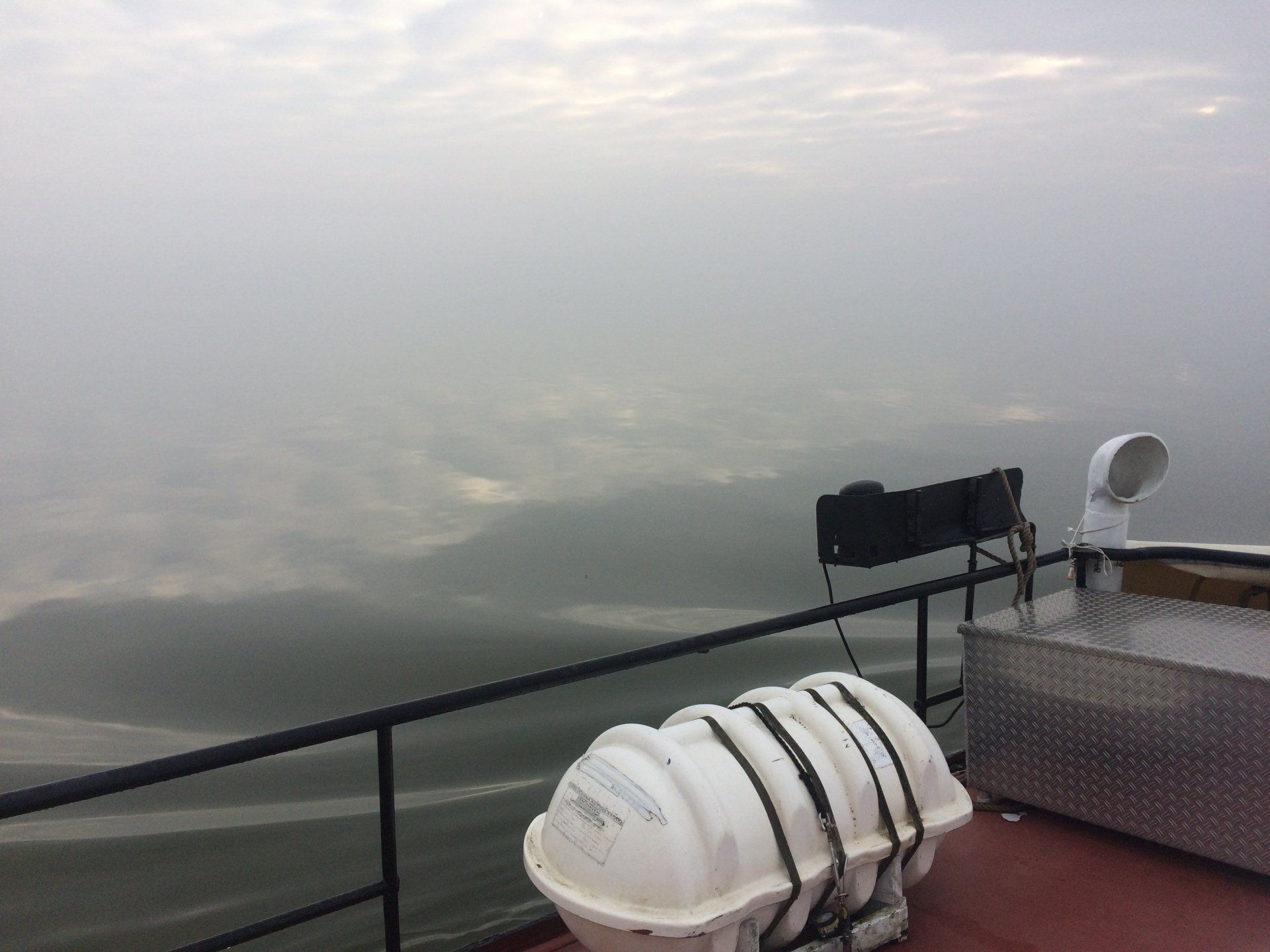 Misty view from the deck with visible safety gear, fog over the water during a Dutch sailing trip.