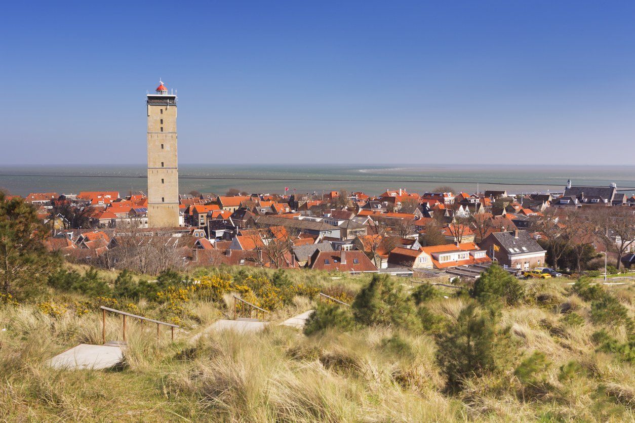 Brandaris lighthouse in West-Terschelling, the Netherlands, rising above colourful roofs and greenery.