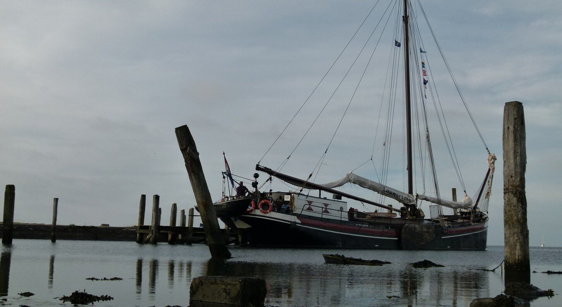 Sailing ship moored by a pier near De Cocksdorp (Texel), with masts and rigging under an overcast sky.