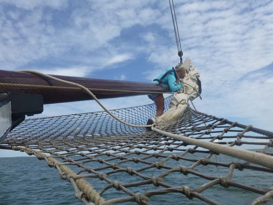 Bow of a traditional sailing ship with rigging and nets, seen from the deck under changing clouds.