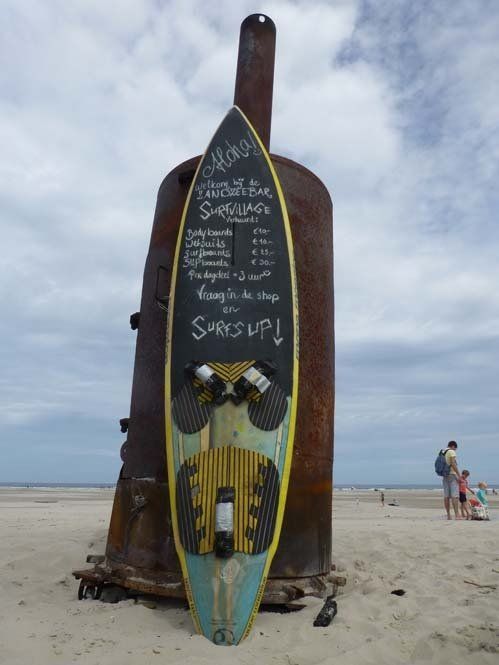 Beach scene on Schiermonnikoog (Dutch Wadden Islands) with a surfboard sign and sunny seaside atmosphere.