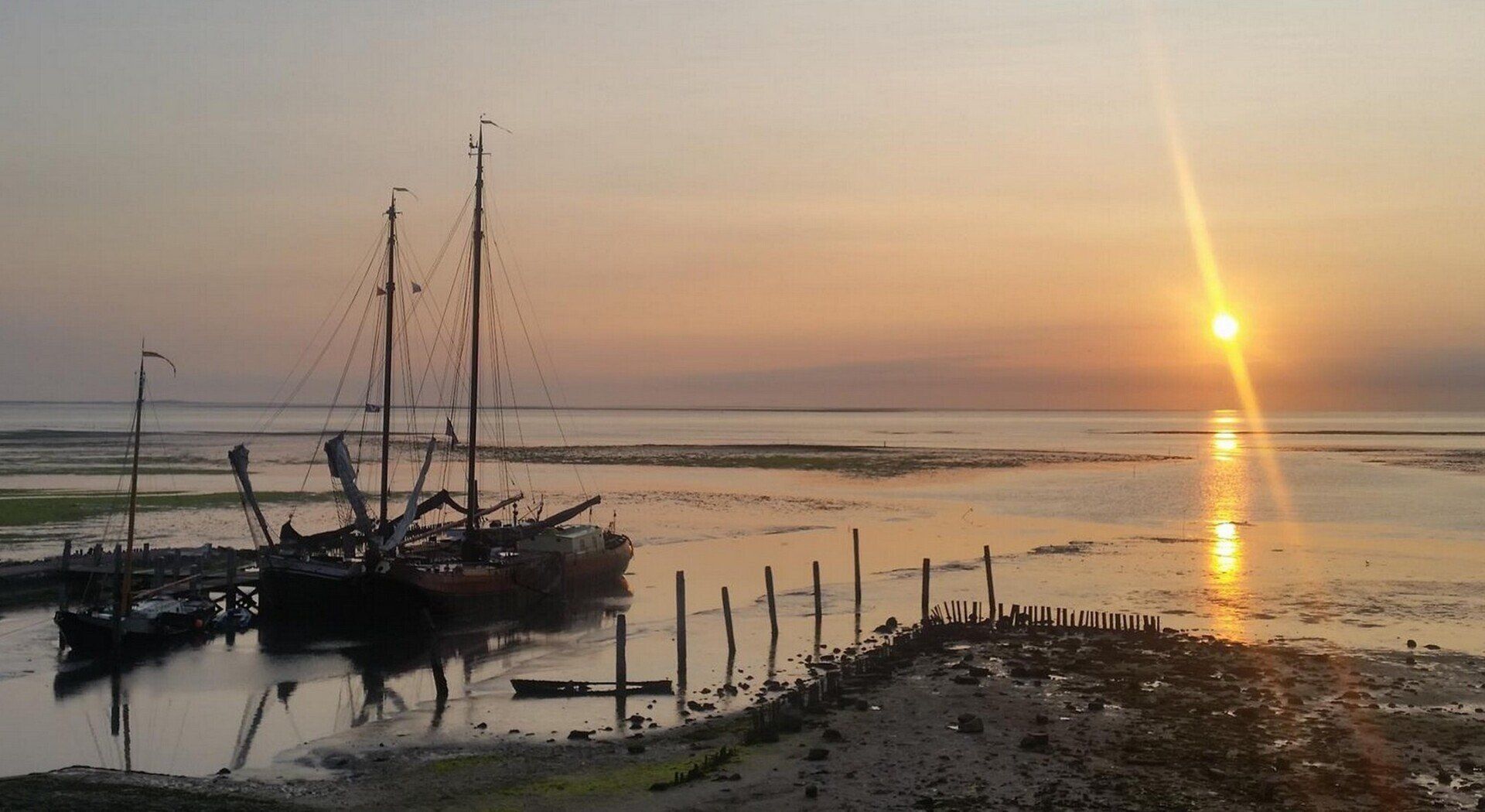 Arriving at harbour at sunset in the Netherlands, orange sky reflected on calm water with silhouettes.